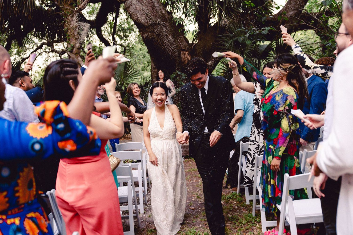 Joyful newlyweds walk through a confetti shower as guests celebrate their outdoor garden wedding ceremony.