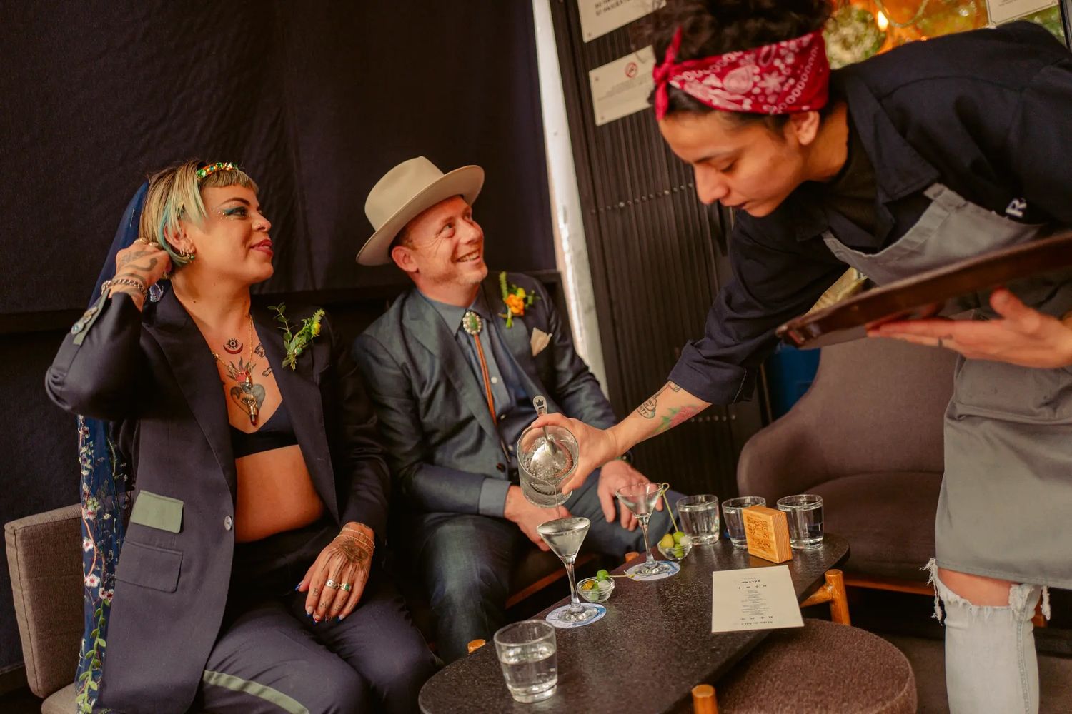Server pouring drinks for smiling couple at colorful wedding reception celebration.
