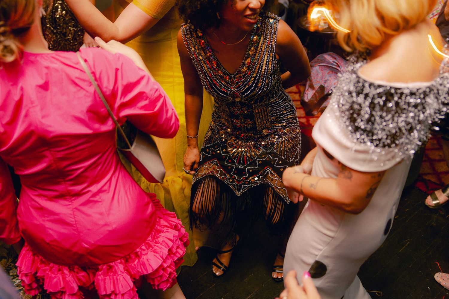 Women in colorful dresses dancing together at a lively evening party or wedding reception.
