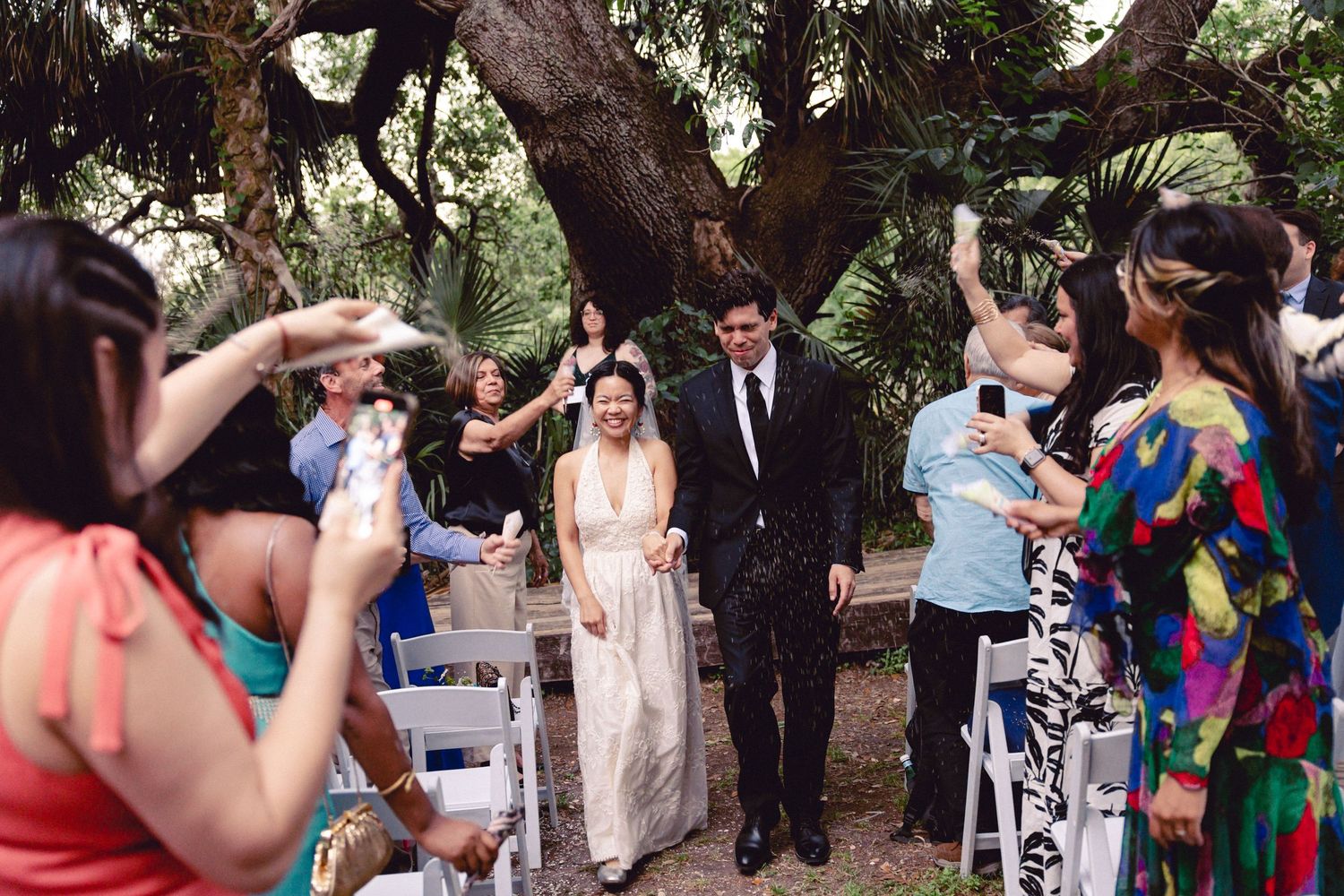 Guests toss confetti on a smiling bride and groom as they exit their outdoor garden wedding ceremony.
