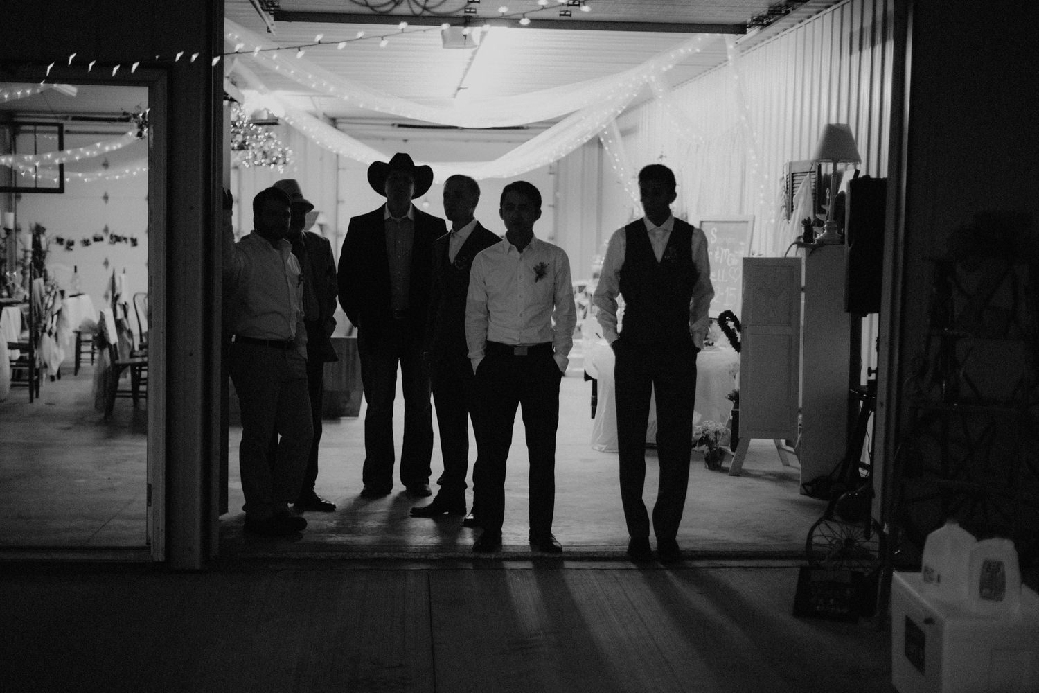 Groomsmen silhouetted in a doorway in a dramatic black and white wedding party portrait.