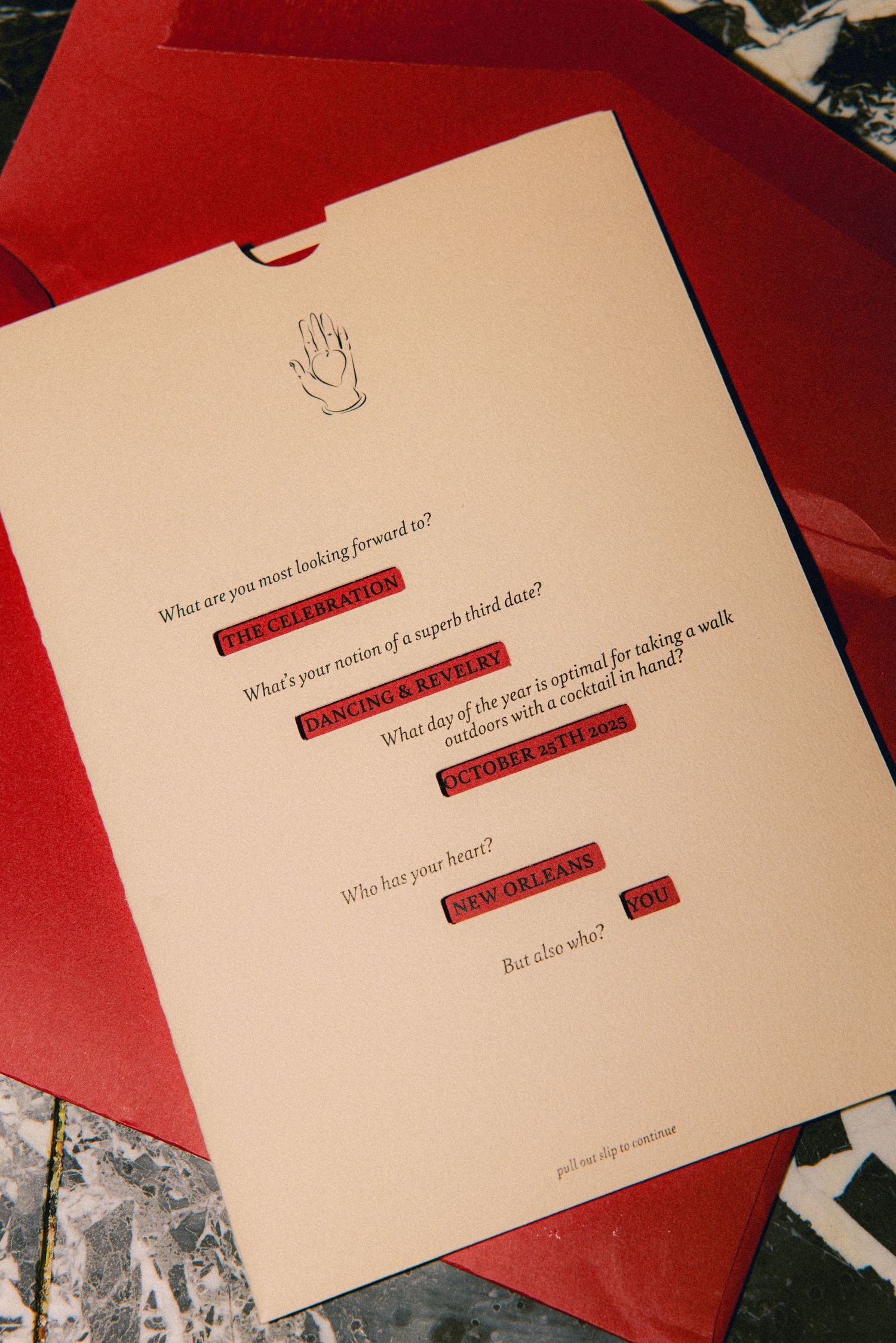 Elegant cream wedding invitation with red accents featuring New Orleans themed questions on marble surface.