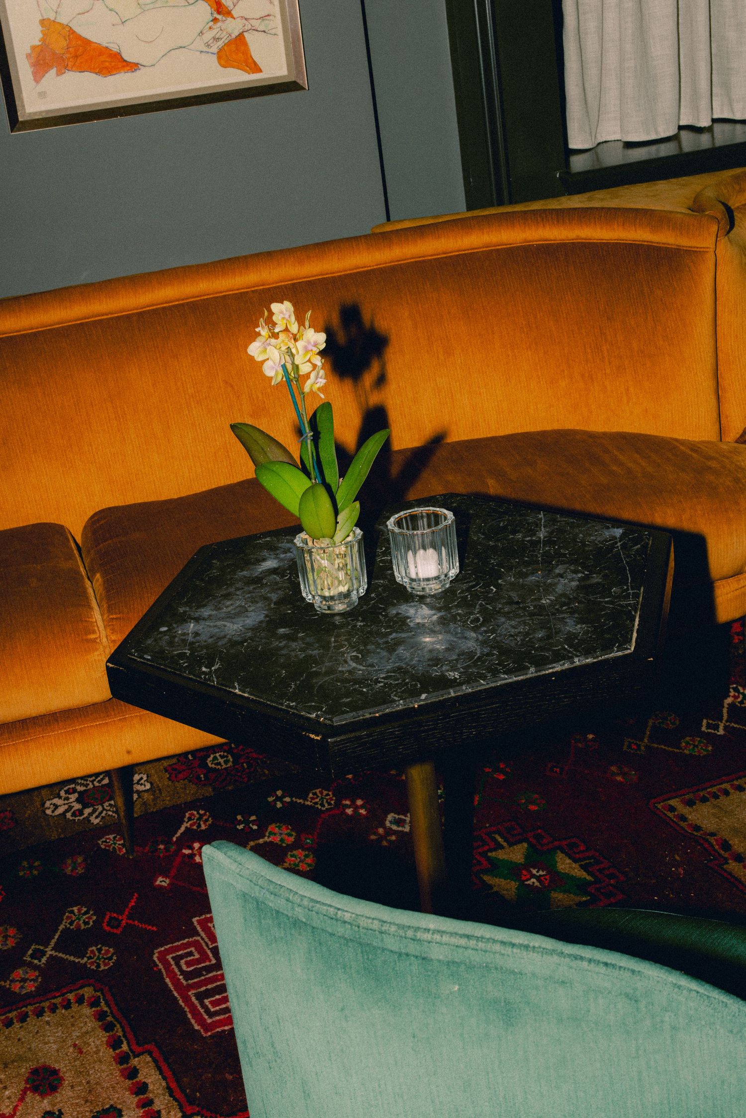 Elegant black marble table with orchid and candle on patterned rug beside gold velvet sofa.