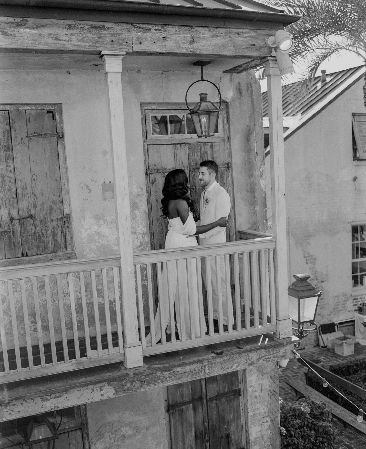 Bride and groom embracing on rustic balcony of historic building in black and white wedding photo.