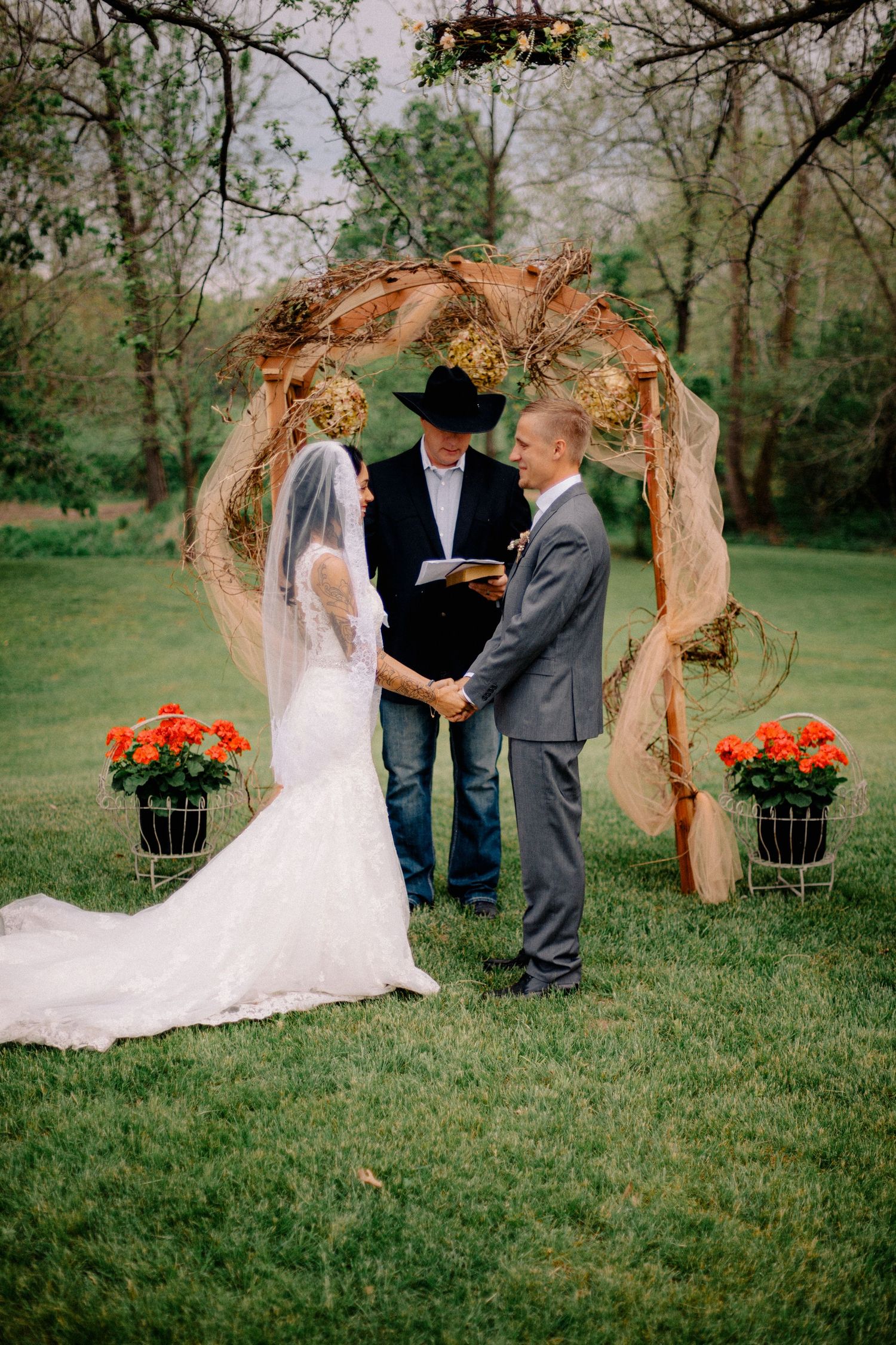 Bride and groom exchange vows under a rustic burlap arch with orange flowers at an outdoor wedding.