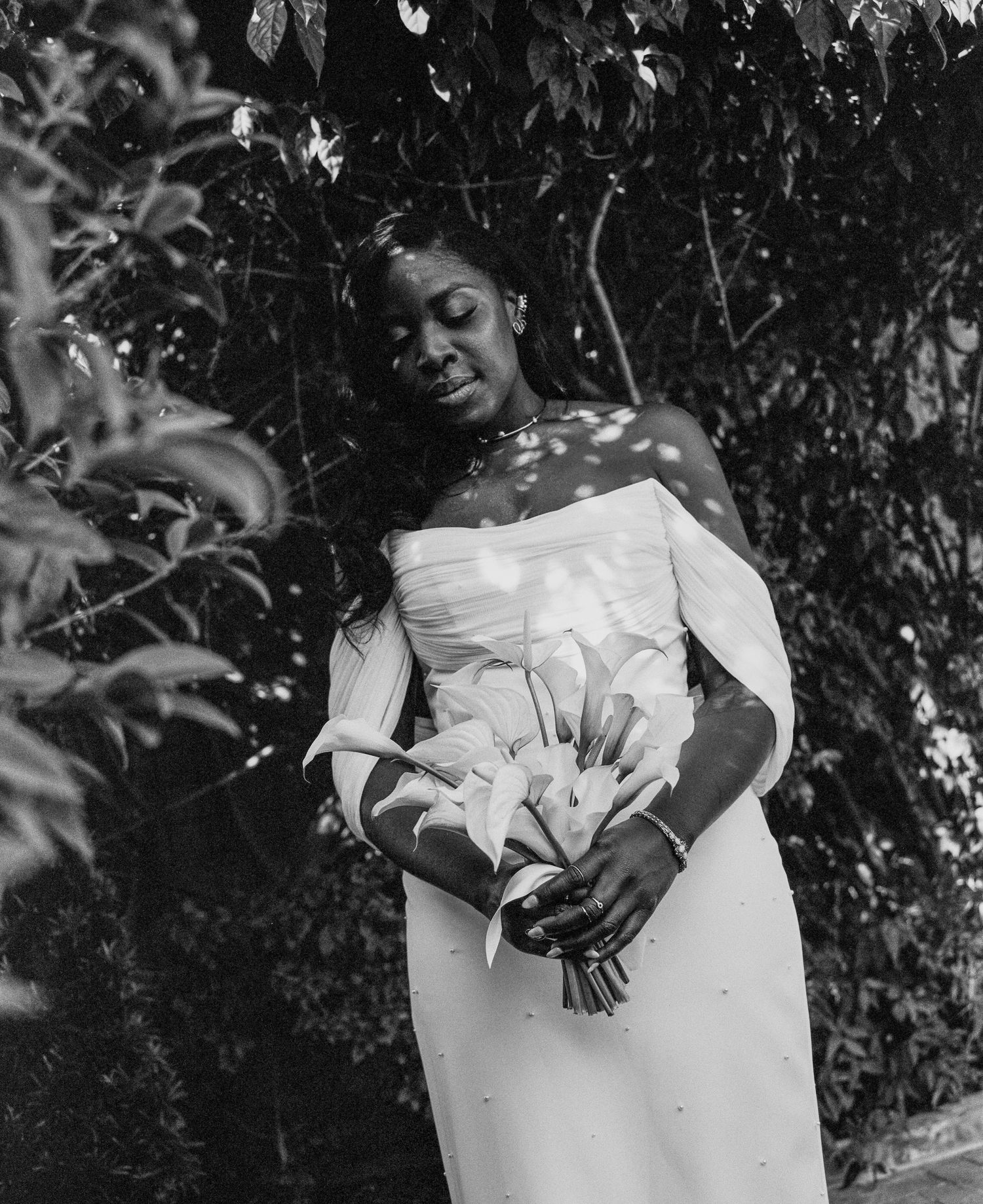 Black and white portrait of a bride in a strapless white gown holding a bouquet of lilies outdoors.