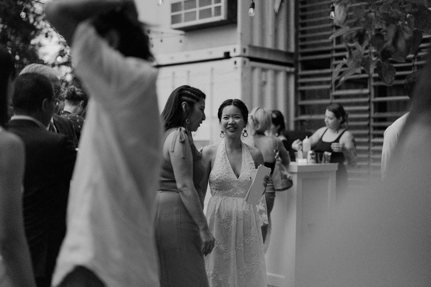 Black and white photo of smiling woman in white dress mingling at outdoor wedding reception.