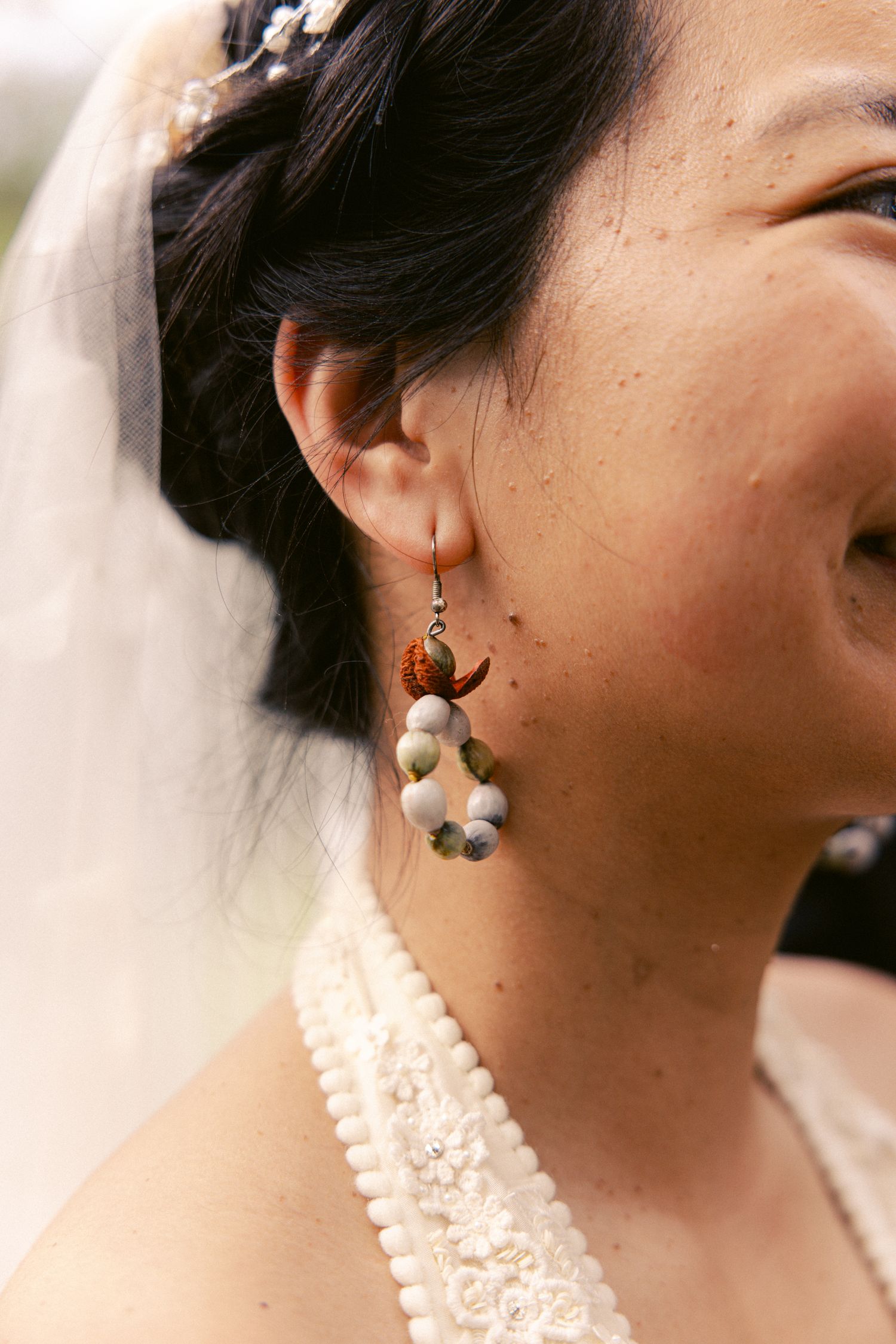 Close-up of a bride wearing a decorative dangle earring, veil, and pearl necklace.