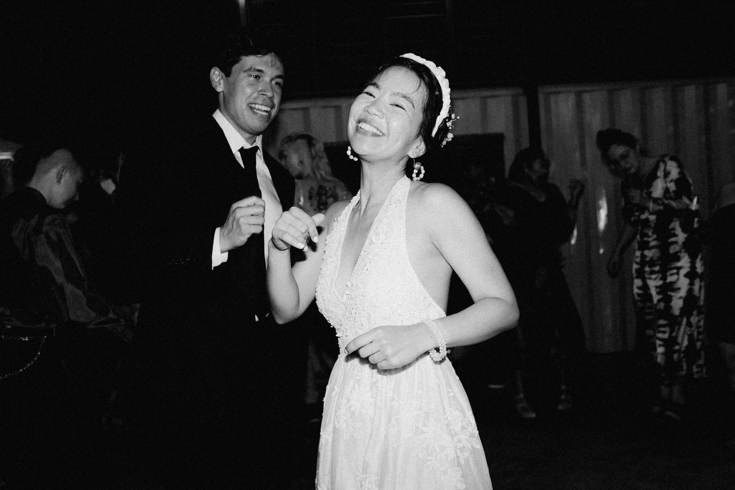 Joyful bride in halter wedding gown laughs while sharing first dance with groom at wedding reception.