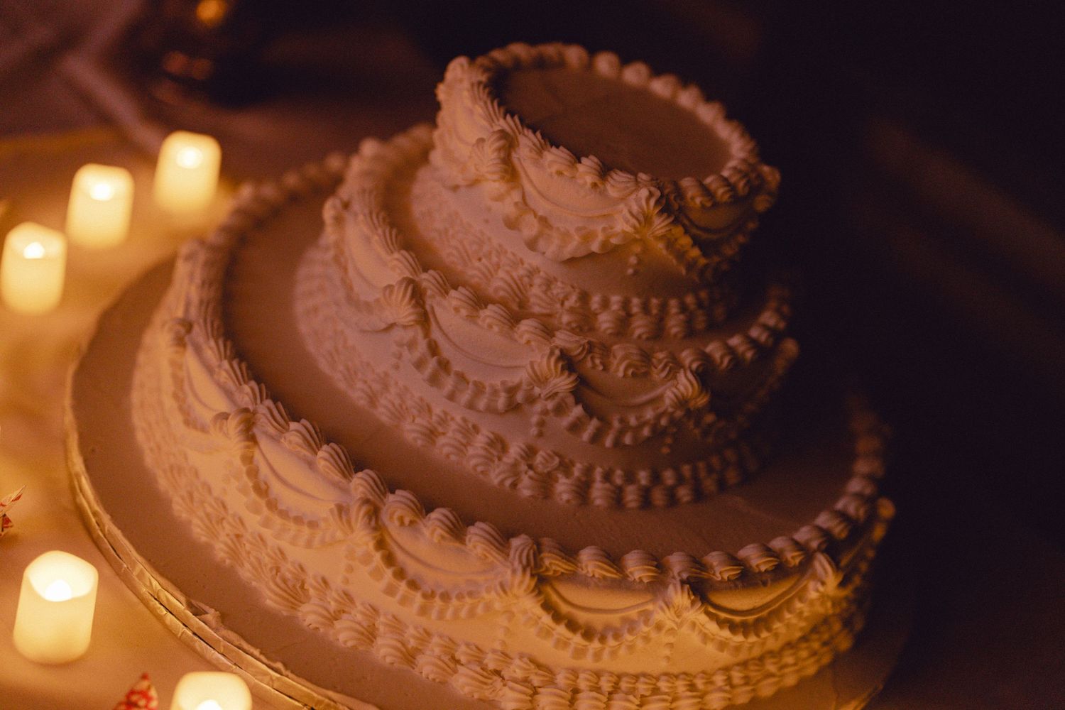 Elegant three-tier white wedding cake decorated with pearls surrounded by glowing candles.
