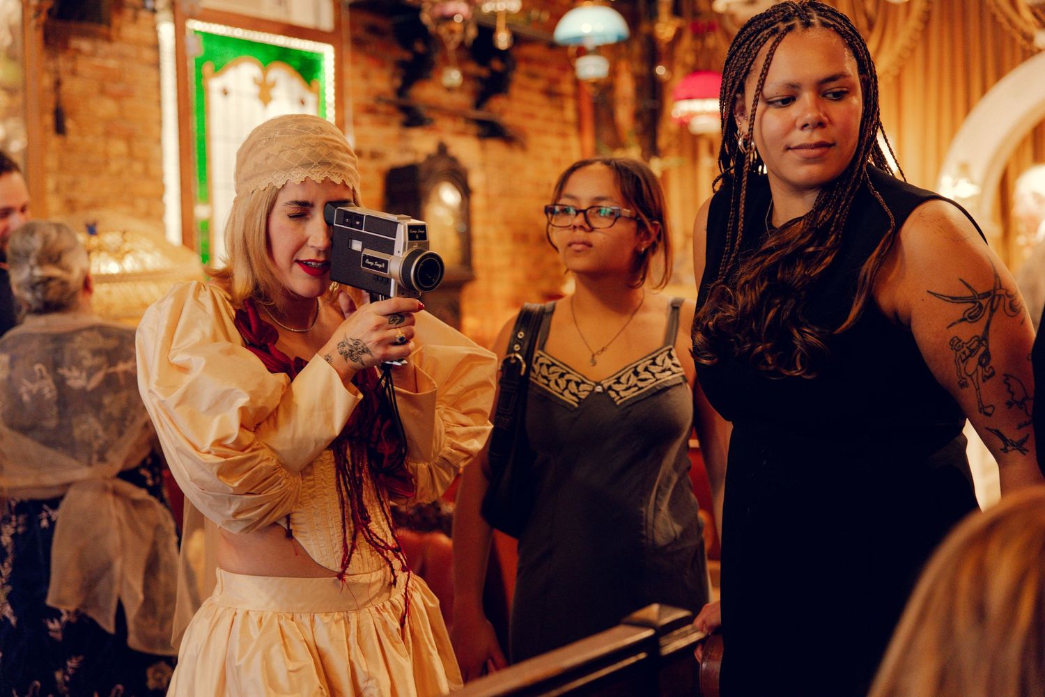 Bride in vintage white gown films guests with a retro camera at a colorful wedding reception.