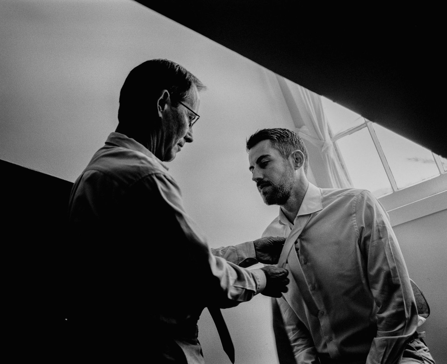 Two men helping each other with neckties in black and white wedding preparation photo.