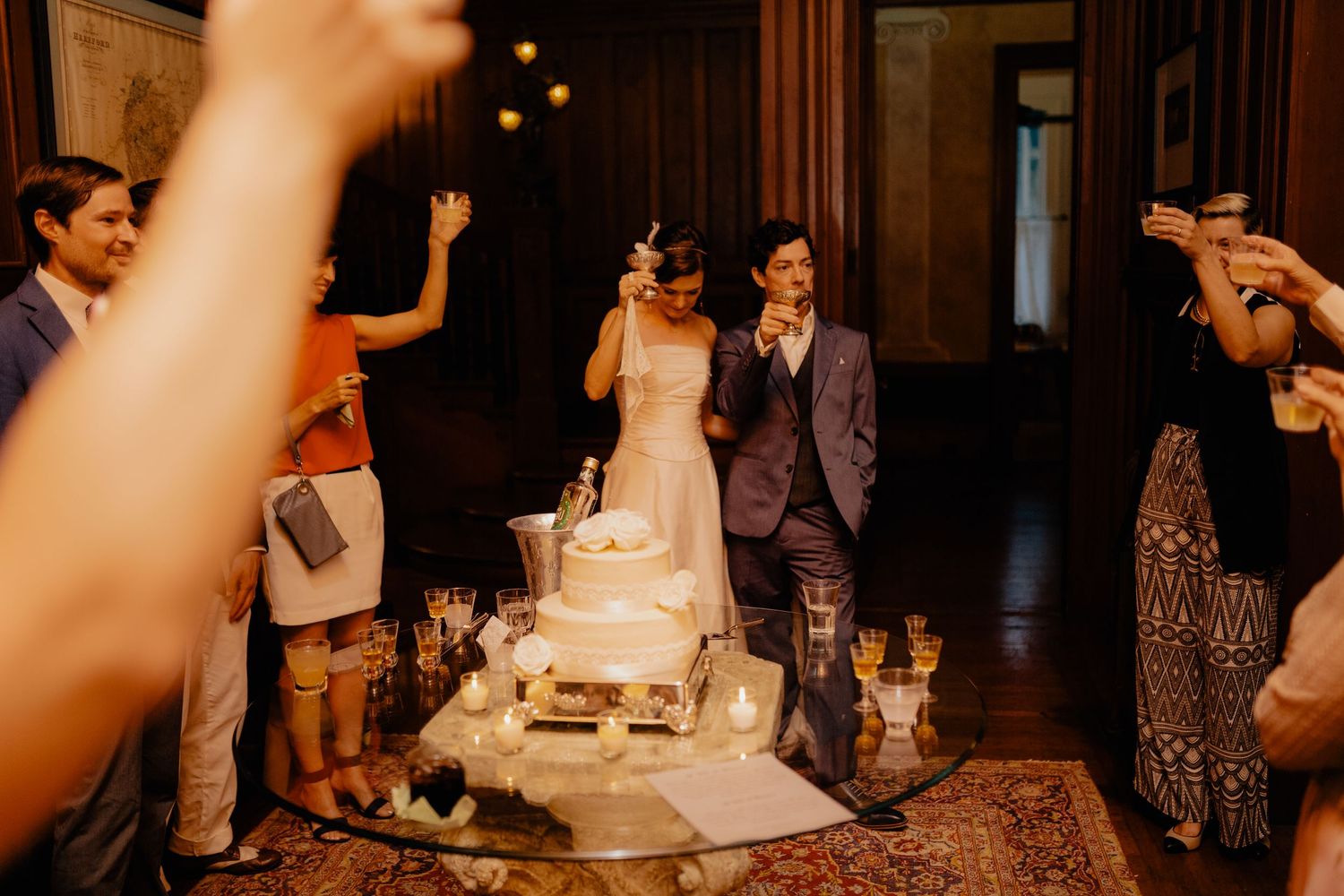 Bride and groom cutting tiered wedding cake surrounded by celebrating guests at elegant reception.