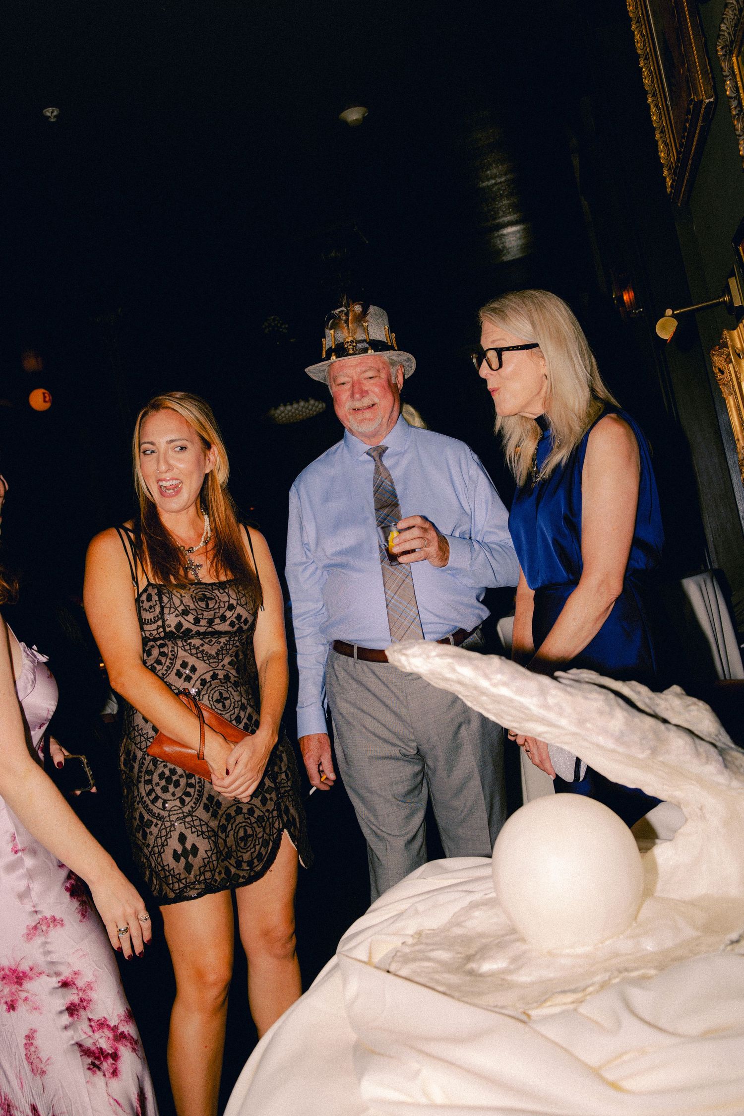 Three guests posing near a white sculptural centerpiece at an elegant evening event.