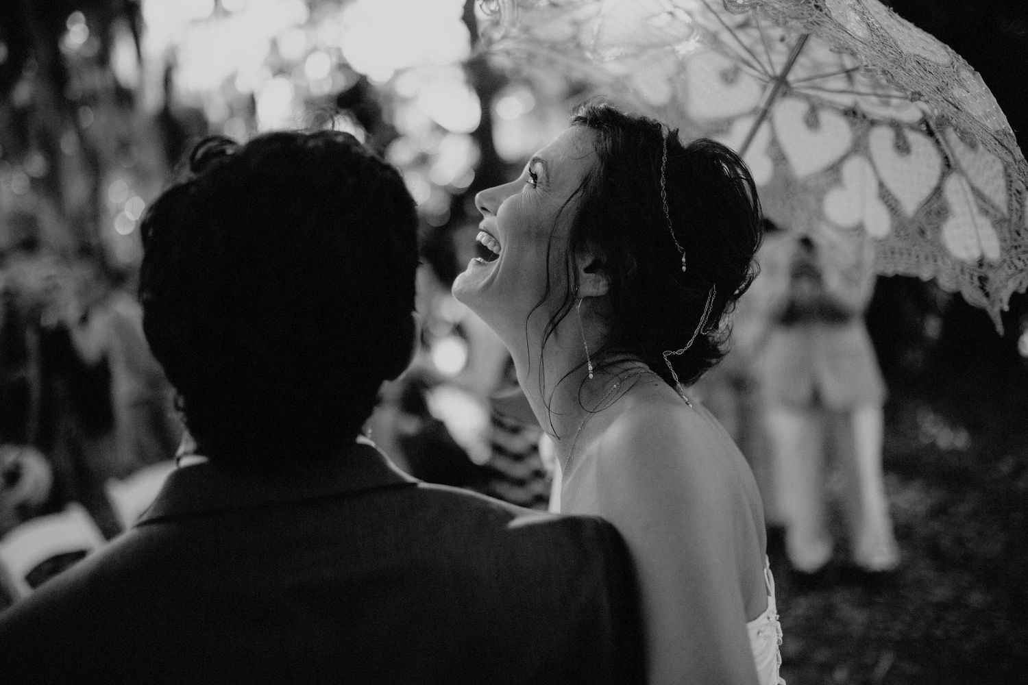 Black and white photo of laughing bride gazing up at groom during romantic outdoor wedding moment.