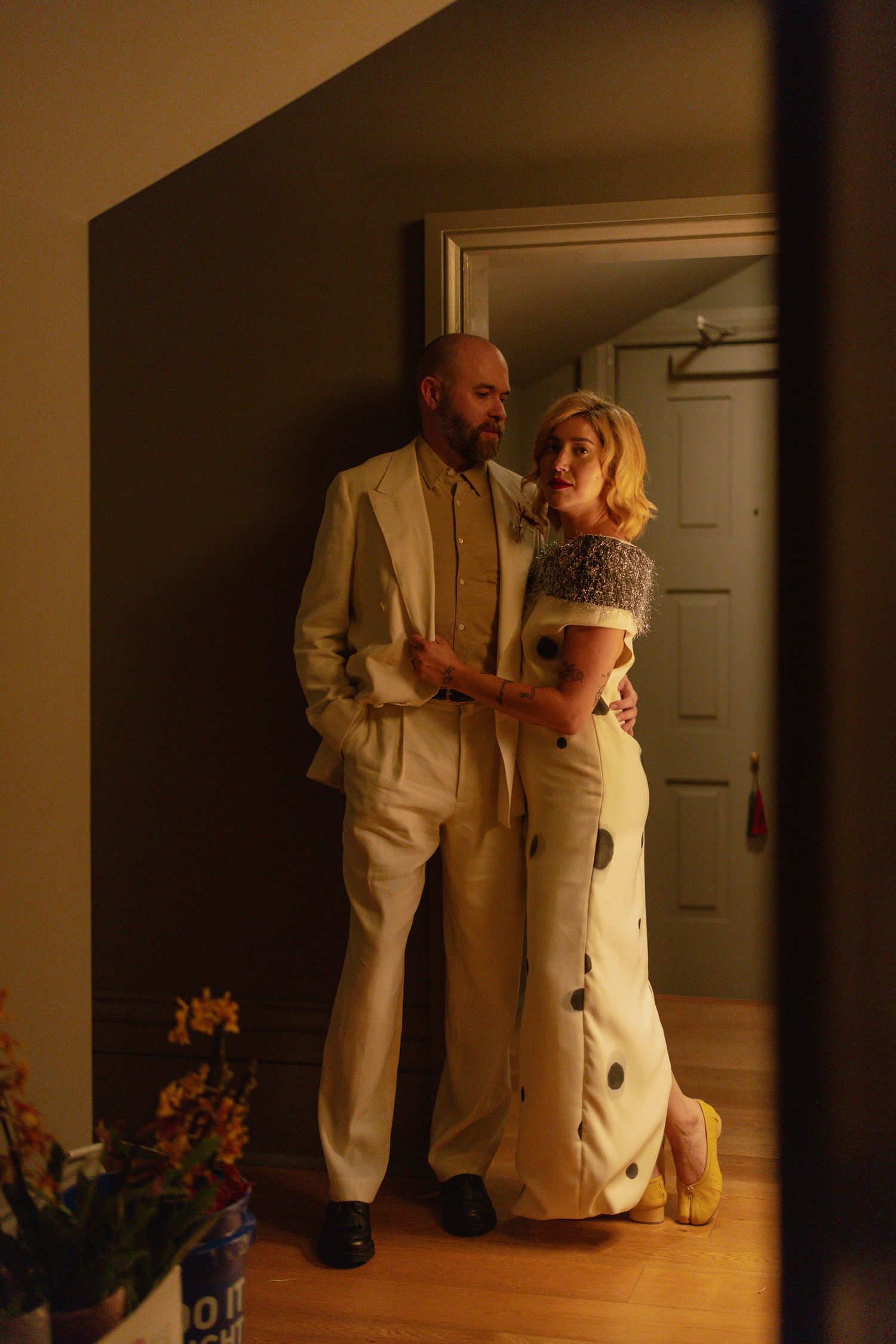Couple in cream wedding attire embrace intimately in warmly lit hallway before their wedding.