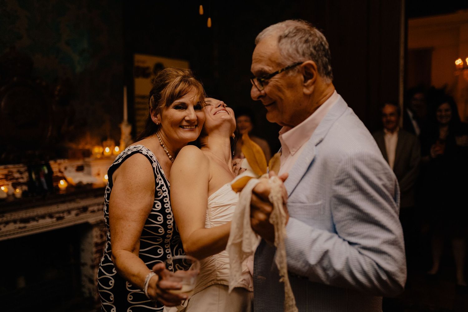 Bride sharing a joyful hug with her parents during a warm wedding reception moment.