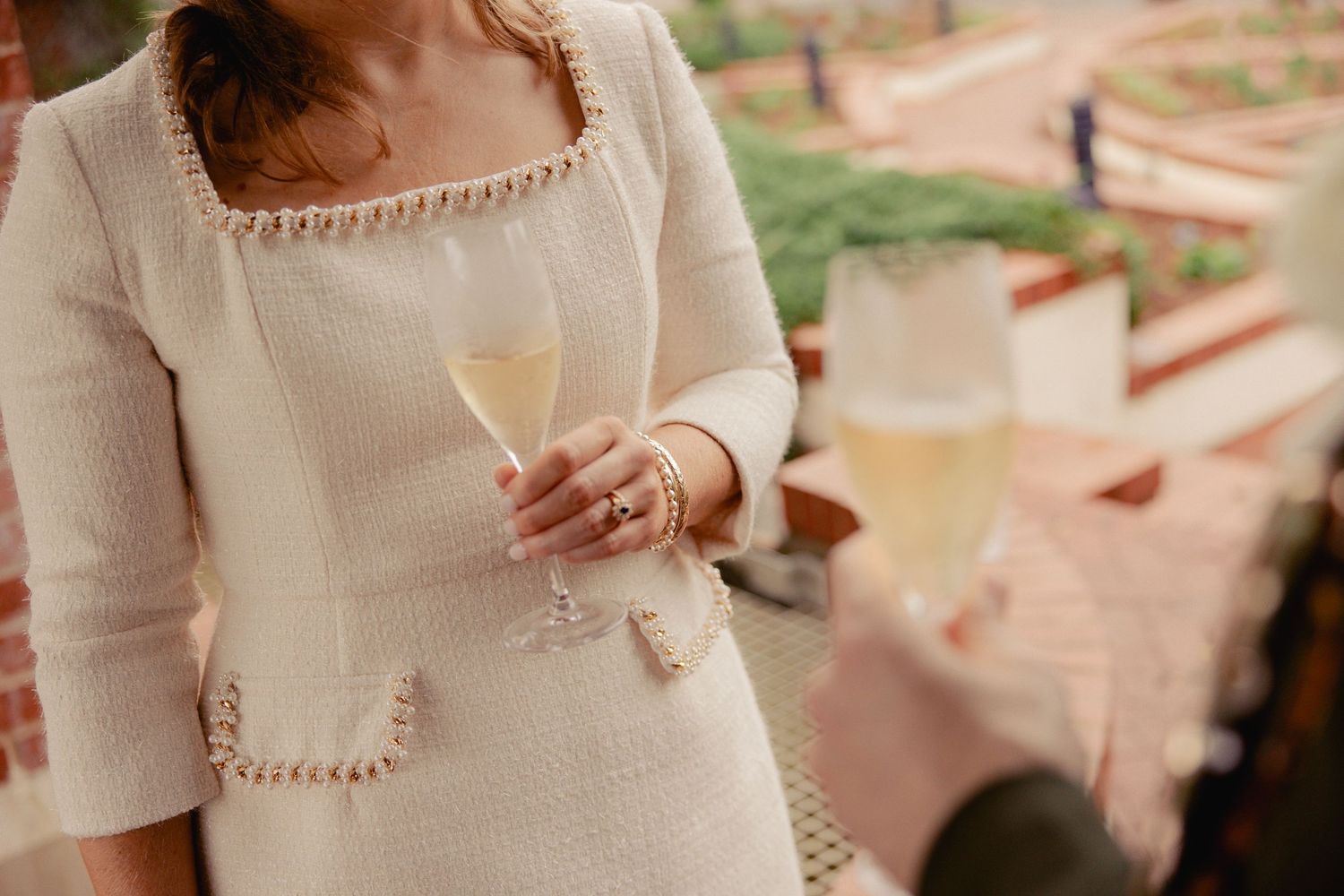 Bride in cream tweed dress holding champagne glass at outdoor wedding reception.