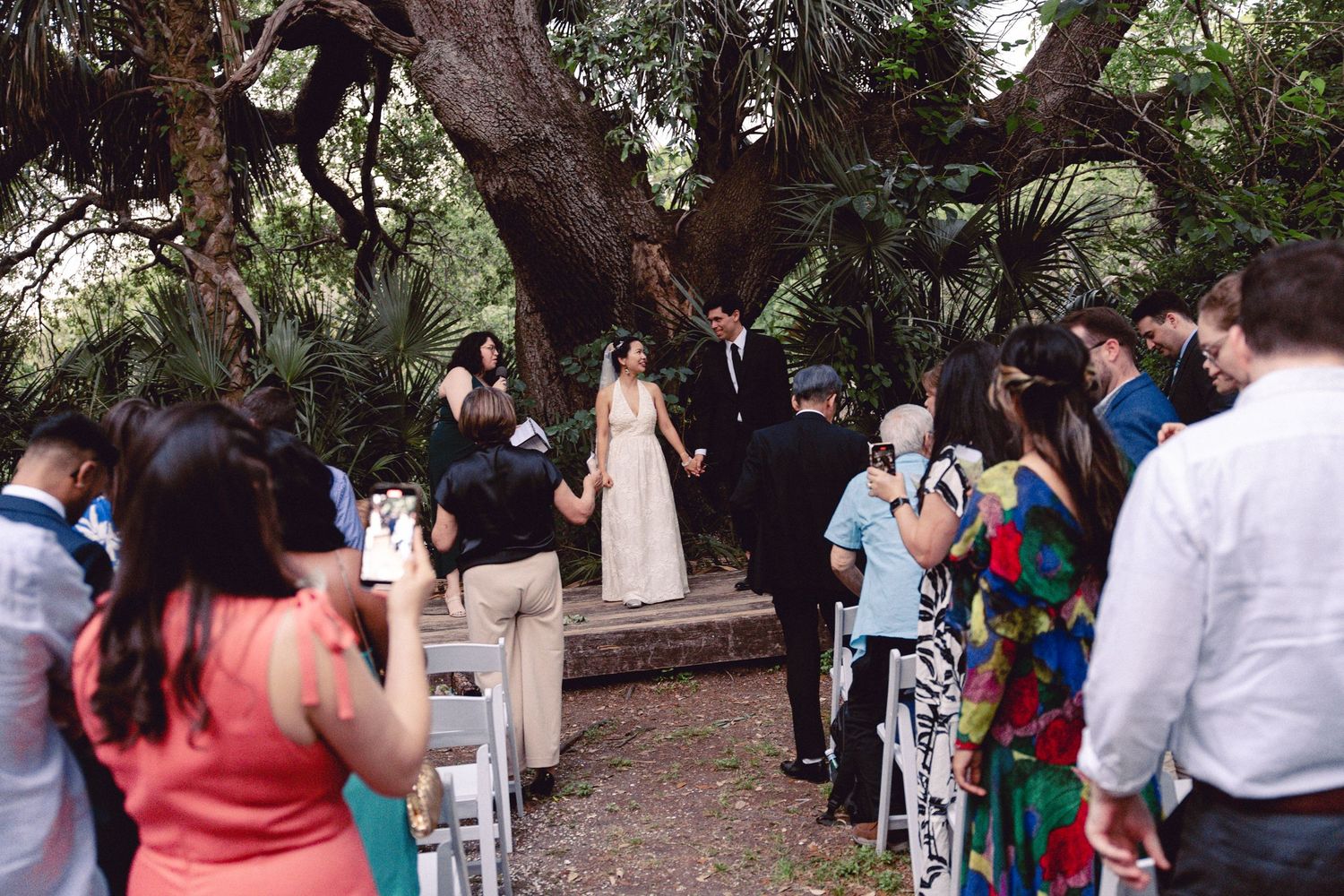 Newlyweds walk hand in hand down the aisle as guests celebrate at an outdoor garden wedding.