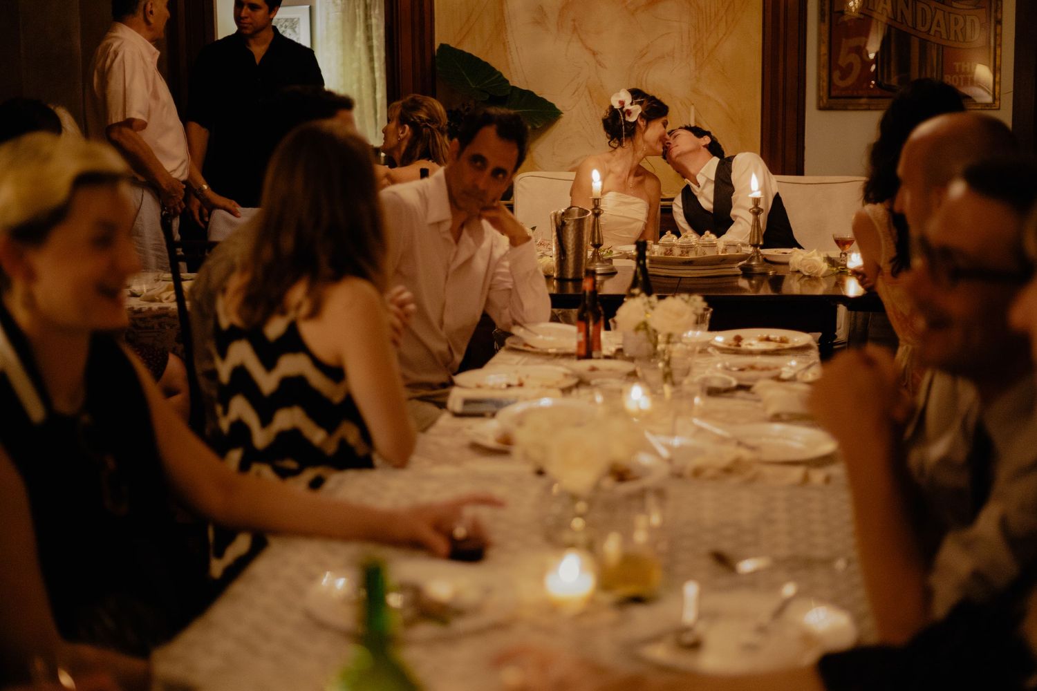Wedding guests enjoying candlelit dinner reception at long elegant table with floral centerpieces.