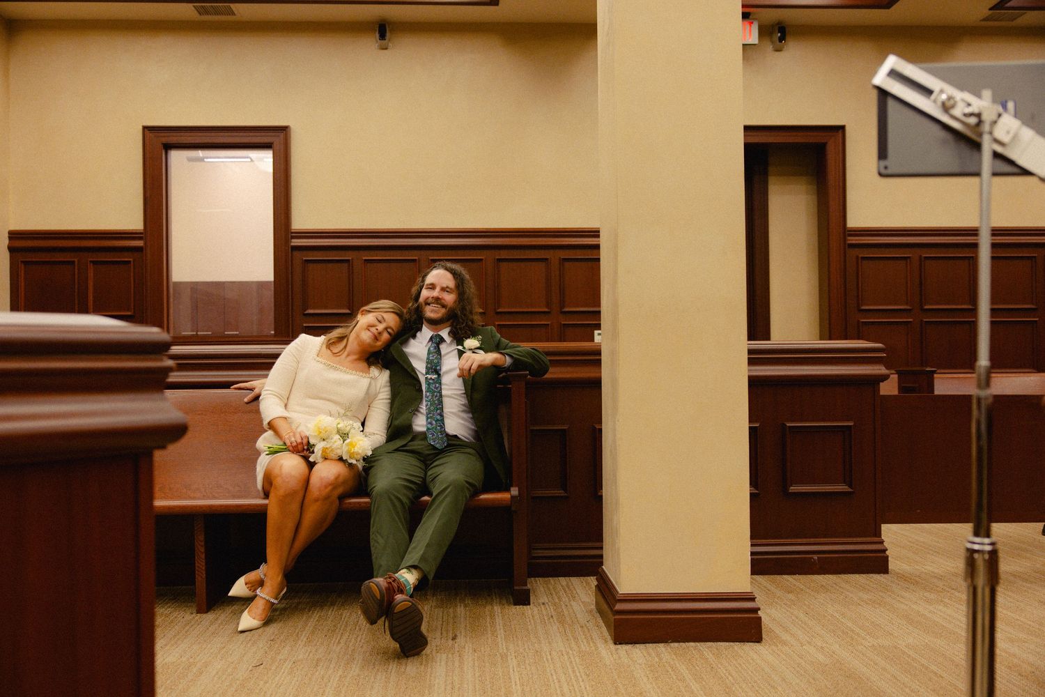Couple relaxing together on courtroom bench during casual courthouse wedding ceremony.