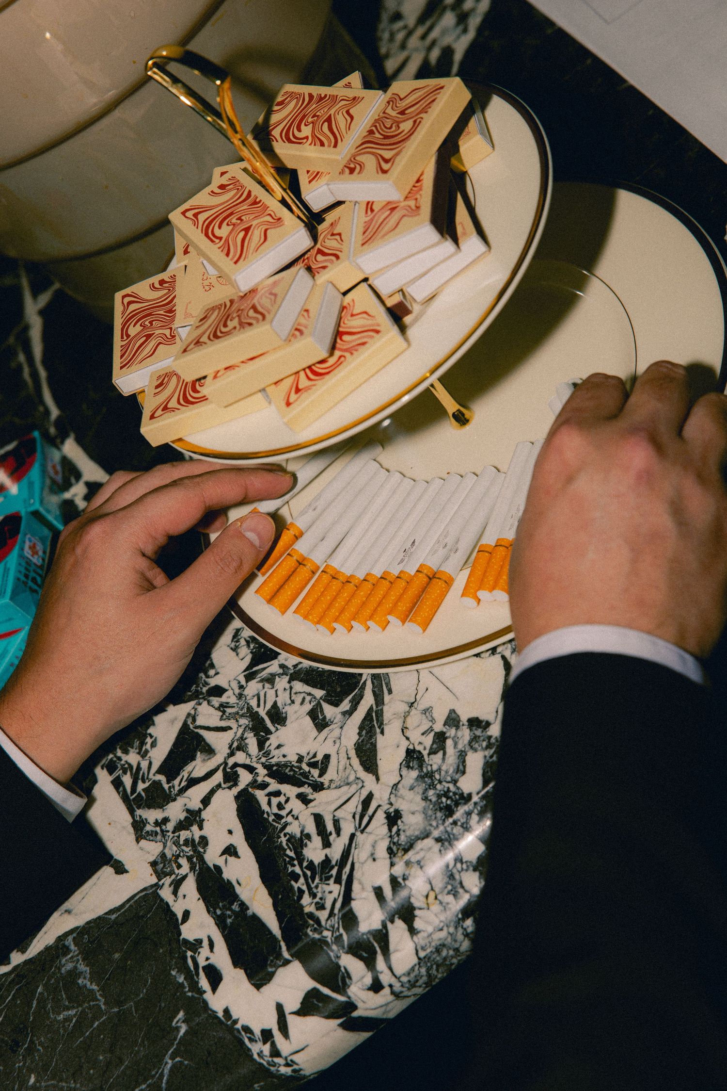 Close-up of hands reaching for cigarettes and matchbooks on tiered display at wedding reception.
