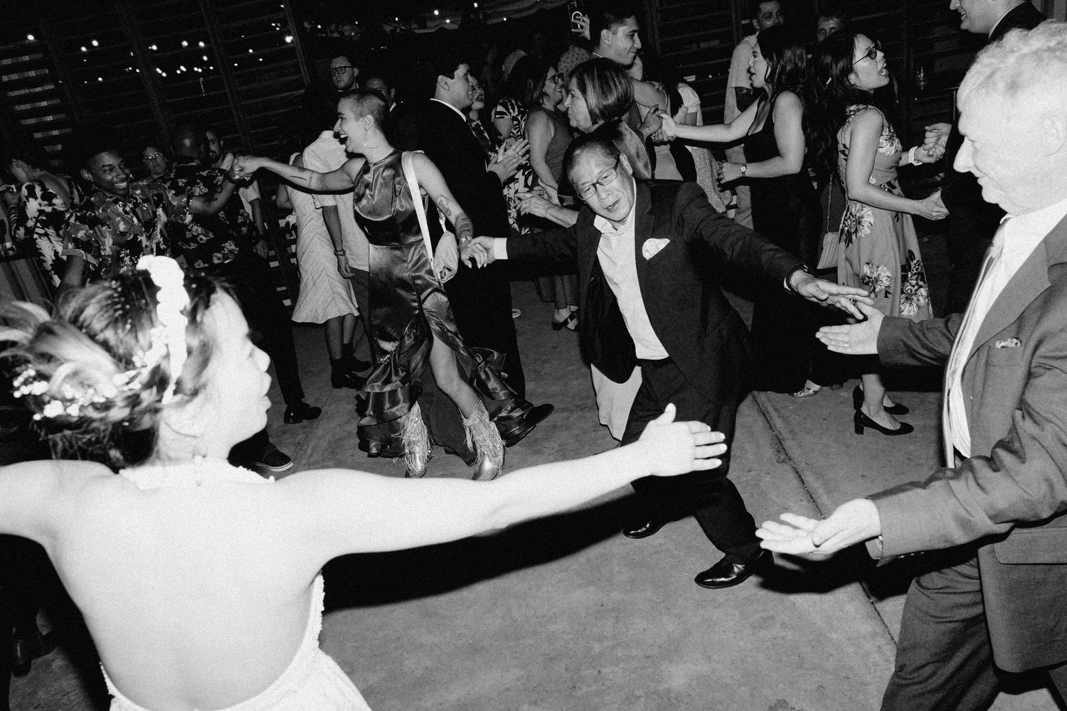 Black and white photo of bride and guests energetically dancing at wedding reception.
