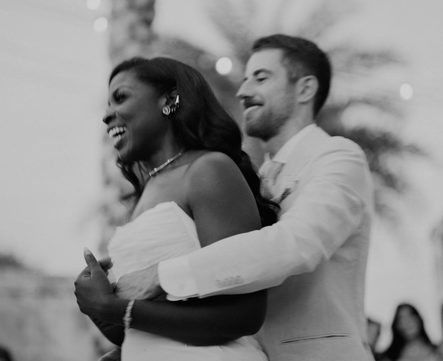 Black and white photo of an interracial couple sharing their first dance at a wedding reception.