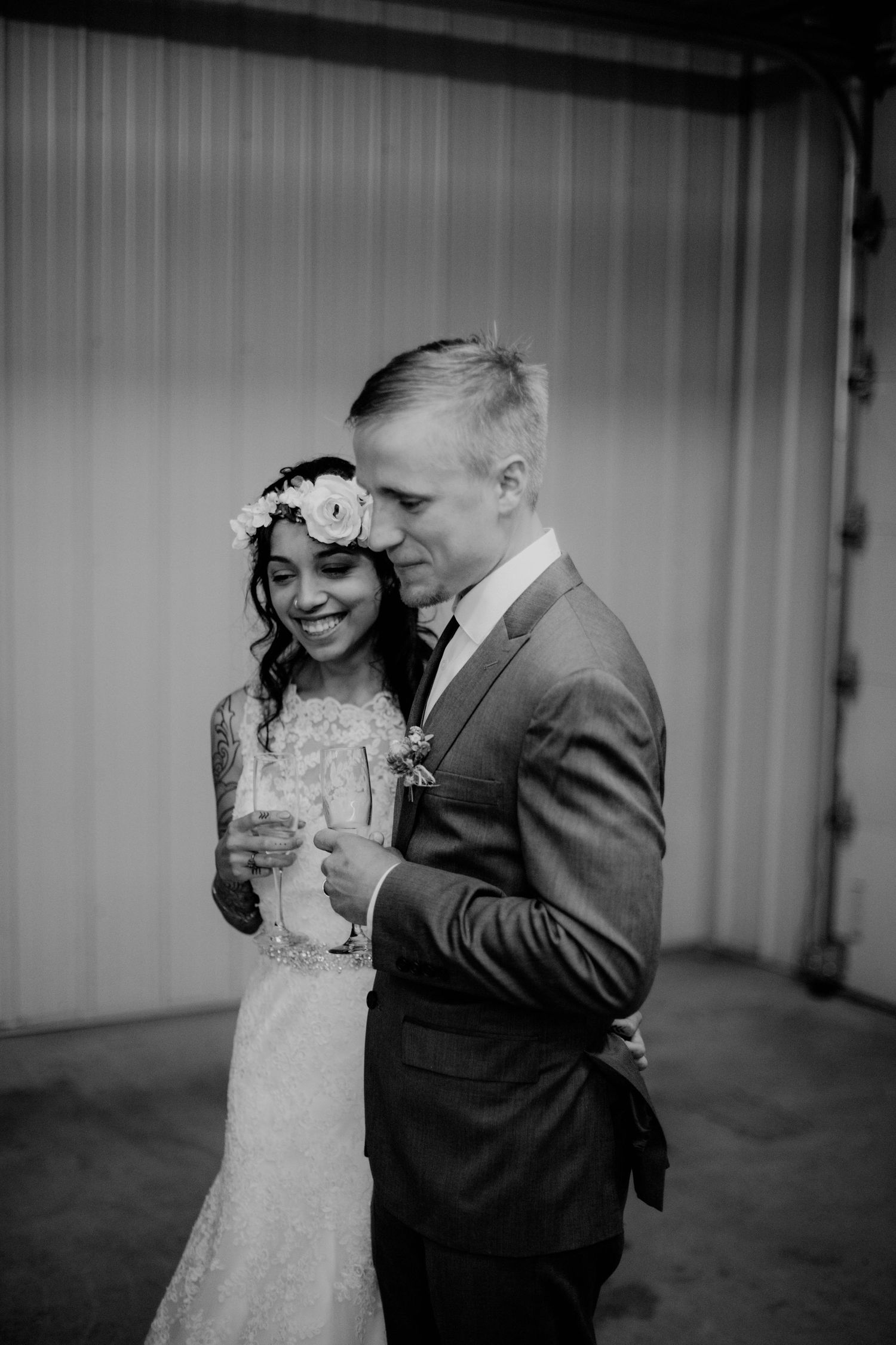 Bride with floral crown and groom in gray suit share champagne in a black and white wedding photo.