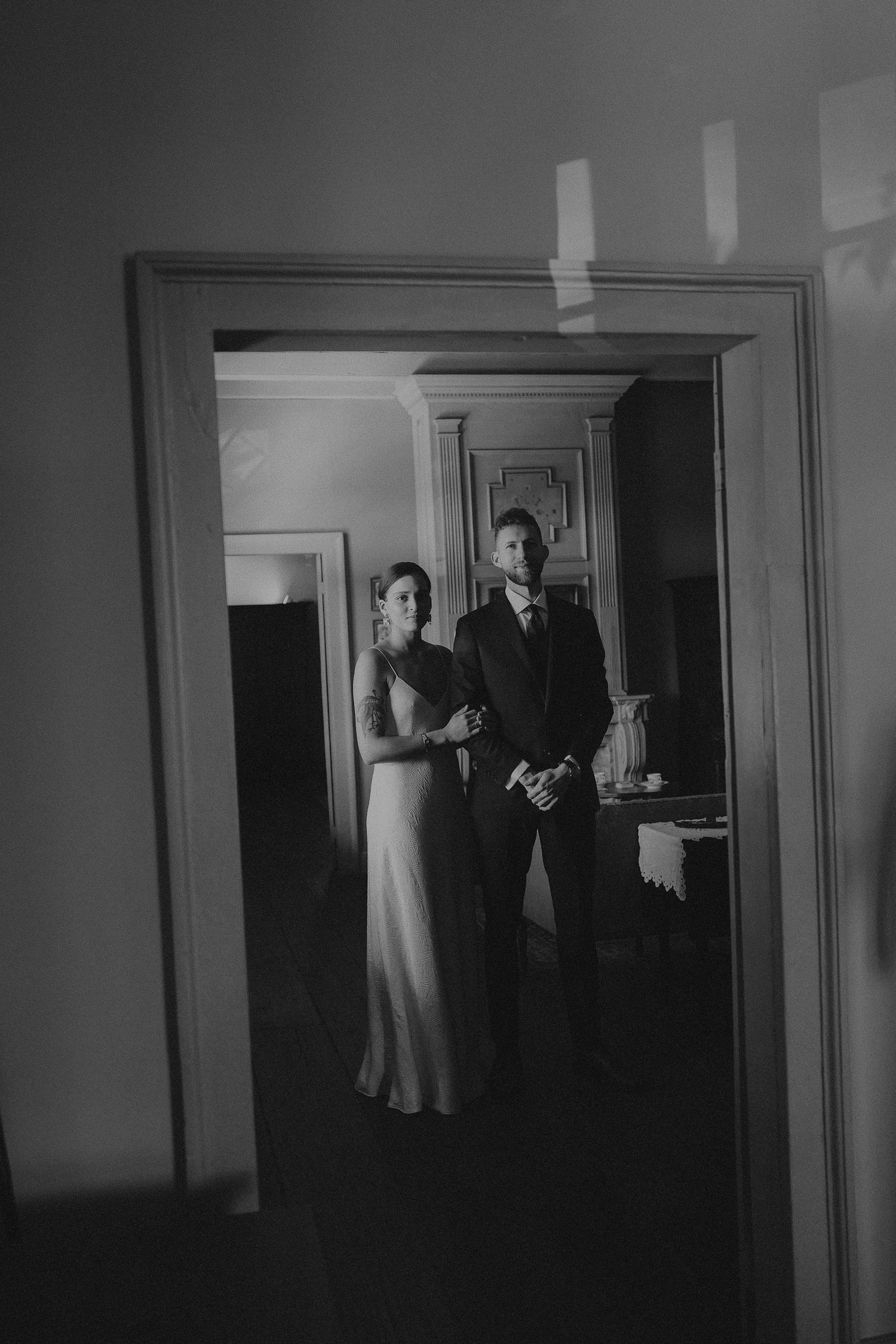 Black and white portrait of bride and groom standing together in a doorway reflection.