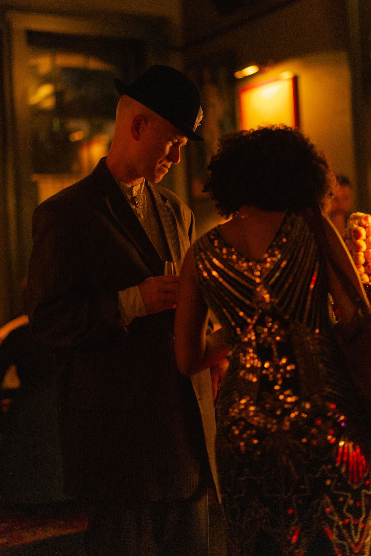 Couple in formal attire sharing an intimate moment at a dimly lit glamorous party.