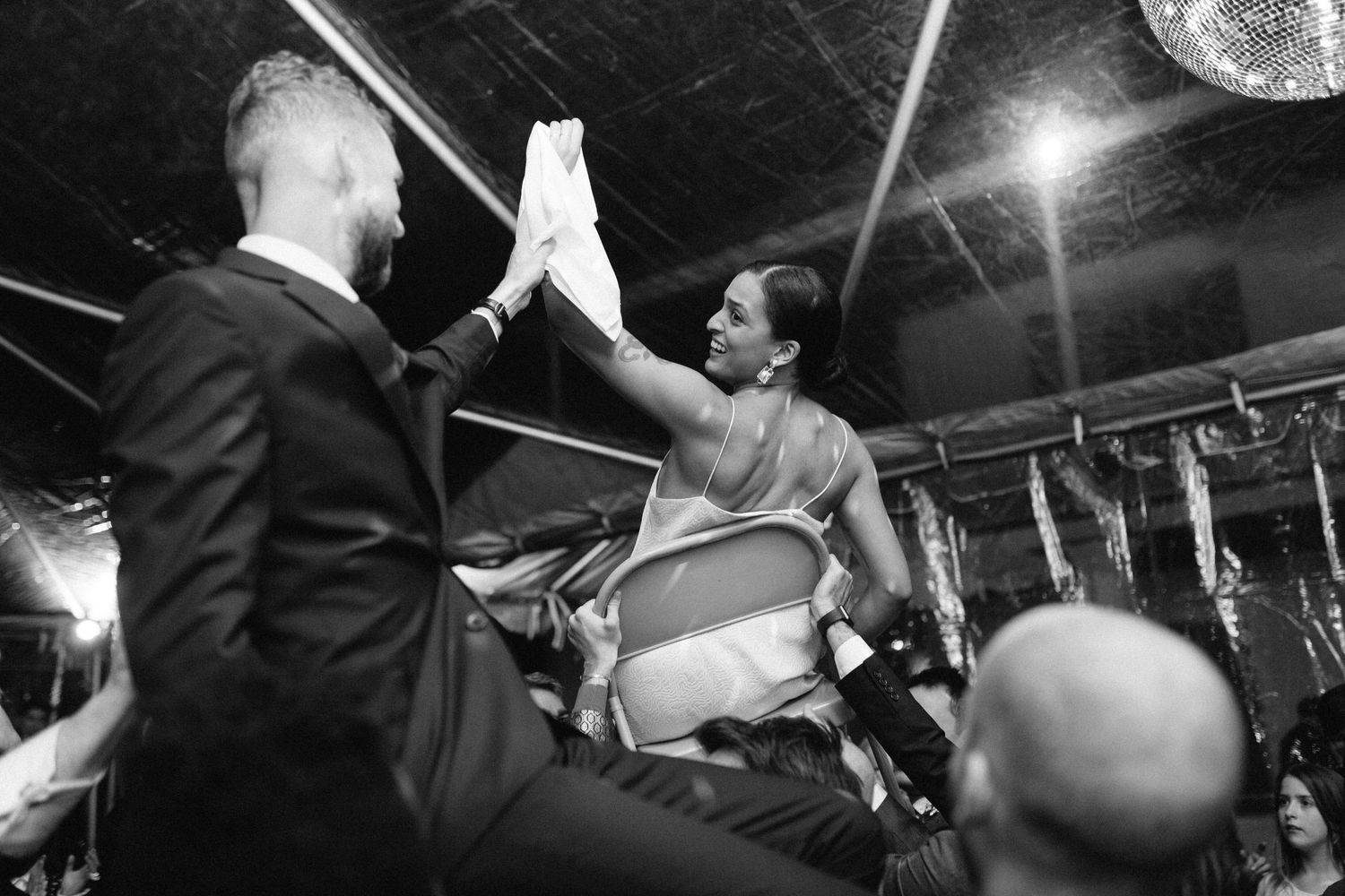 Black and white photo of wedding guests high-fiving at a lively reception party.