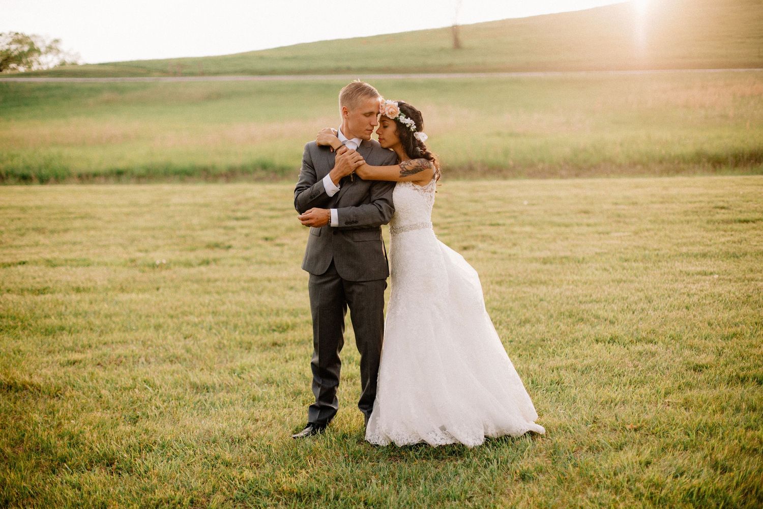 Bride and groom share a romantic dance in a sunlit green field during golden hour.