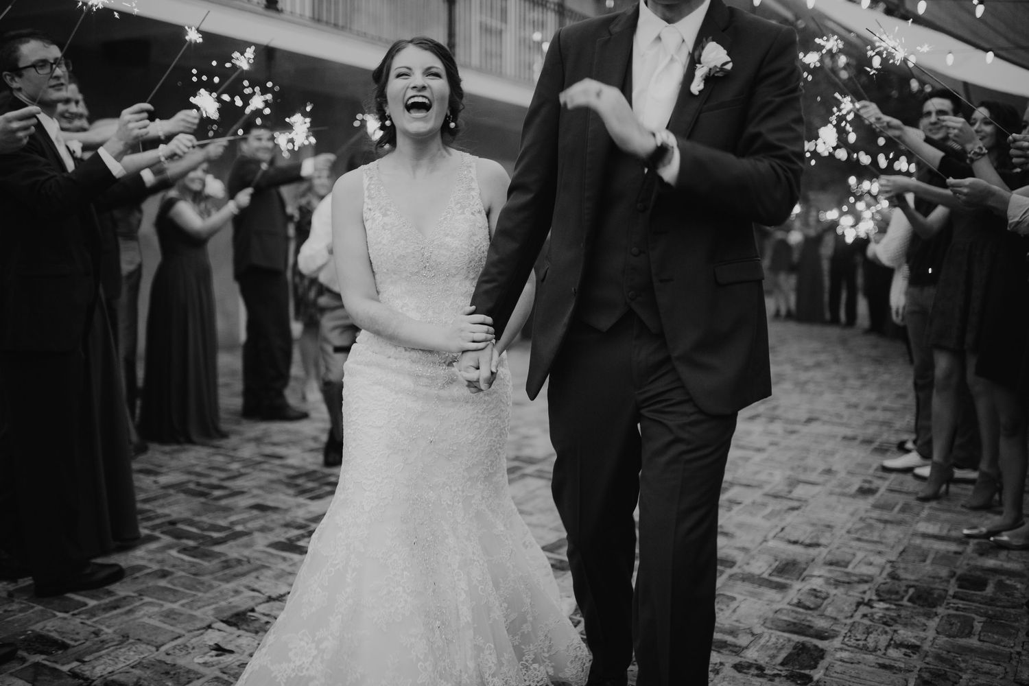 Joyful bride and groom exit through sparkler send-off on cobblestone street at night.