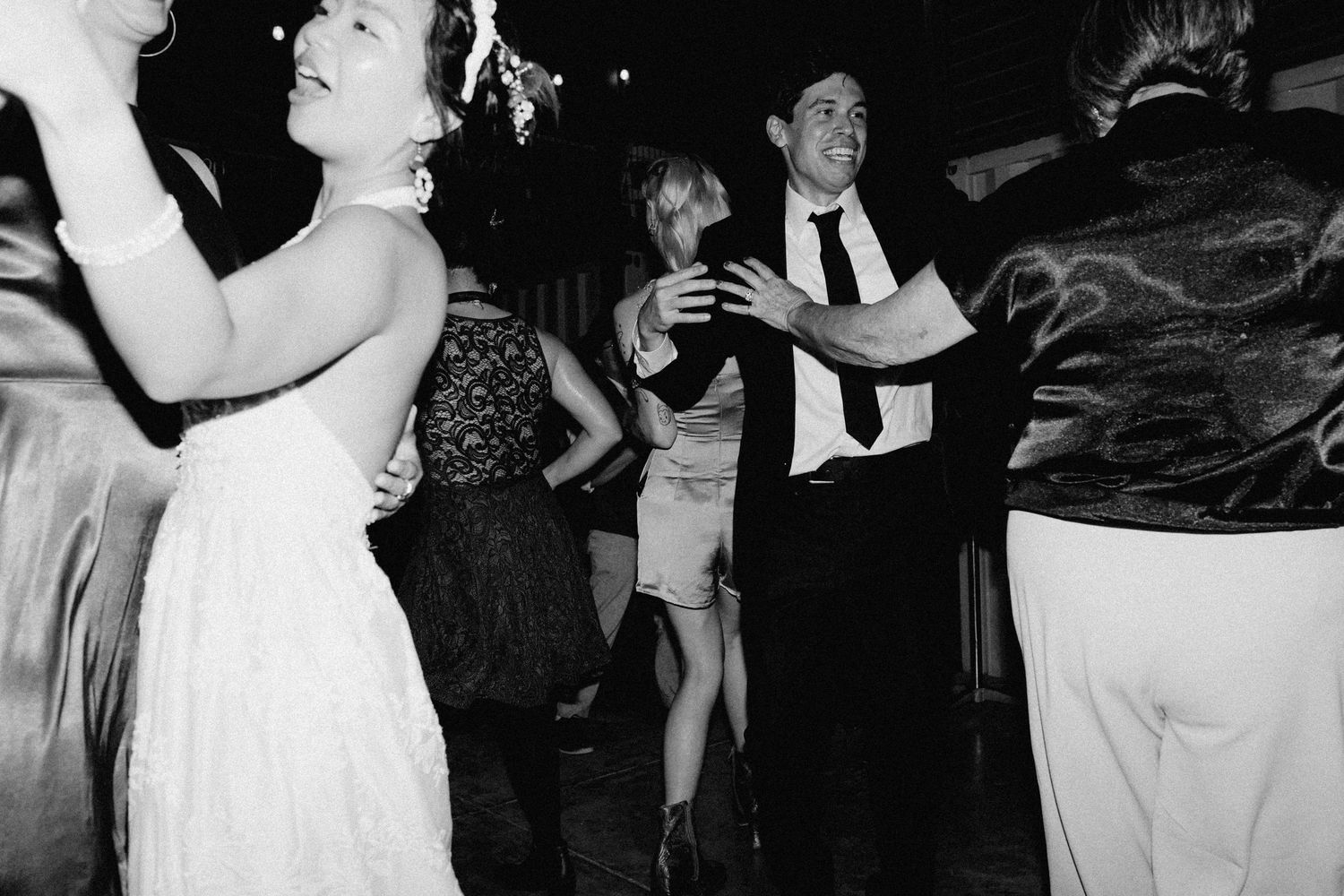 Black and white photo of bride and groom dancing joyfully at wedding reception.
