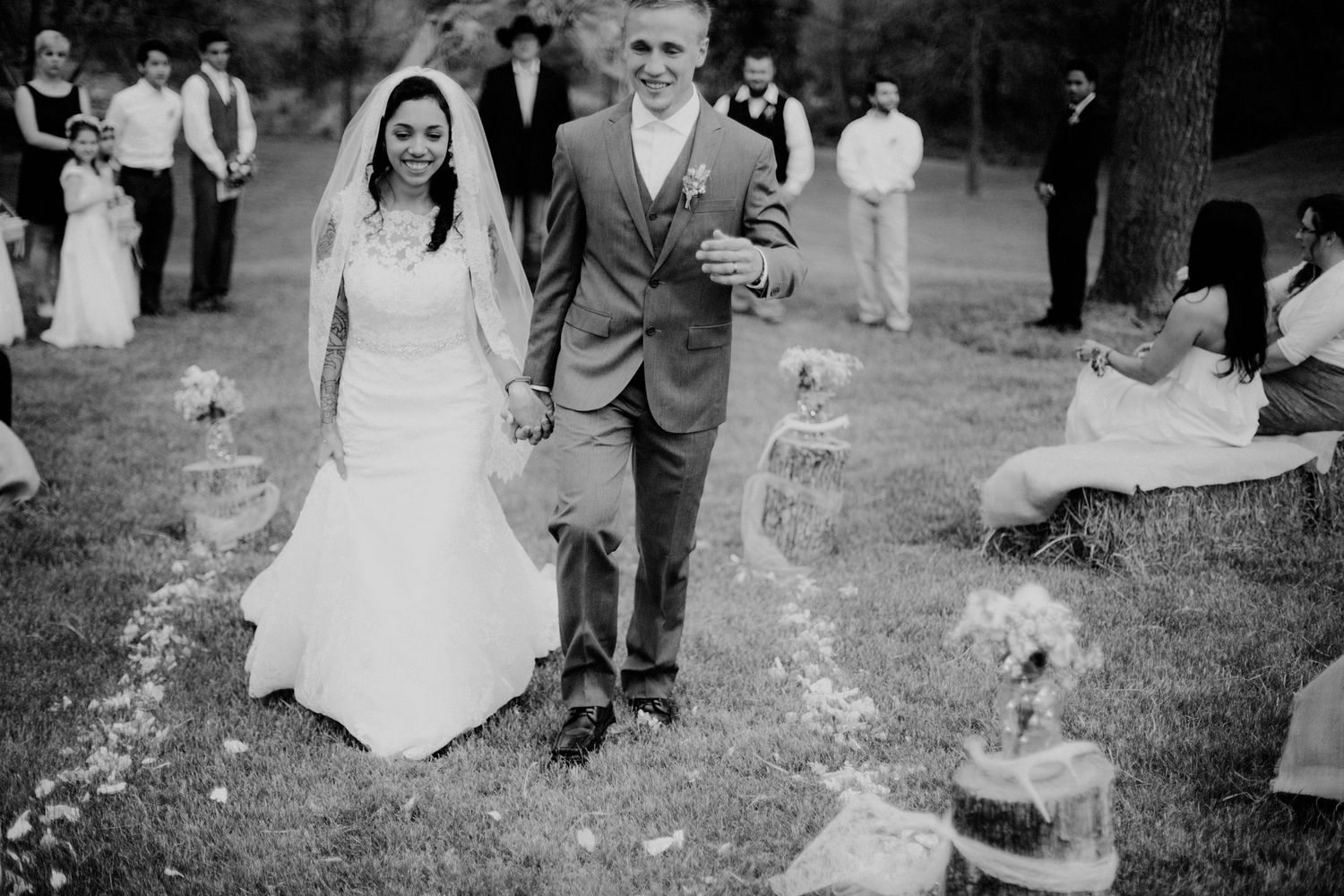 Newlyweds walk hand in hand down the aisle after outdoor garden wedding ceremony in black and white photo.