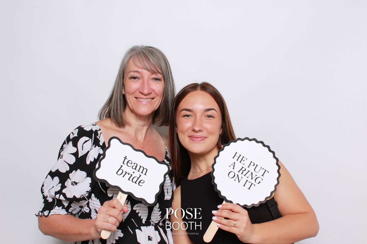 Two people in black and white floral print clothing pose together with props at a photo booth.