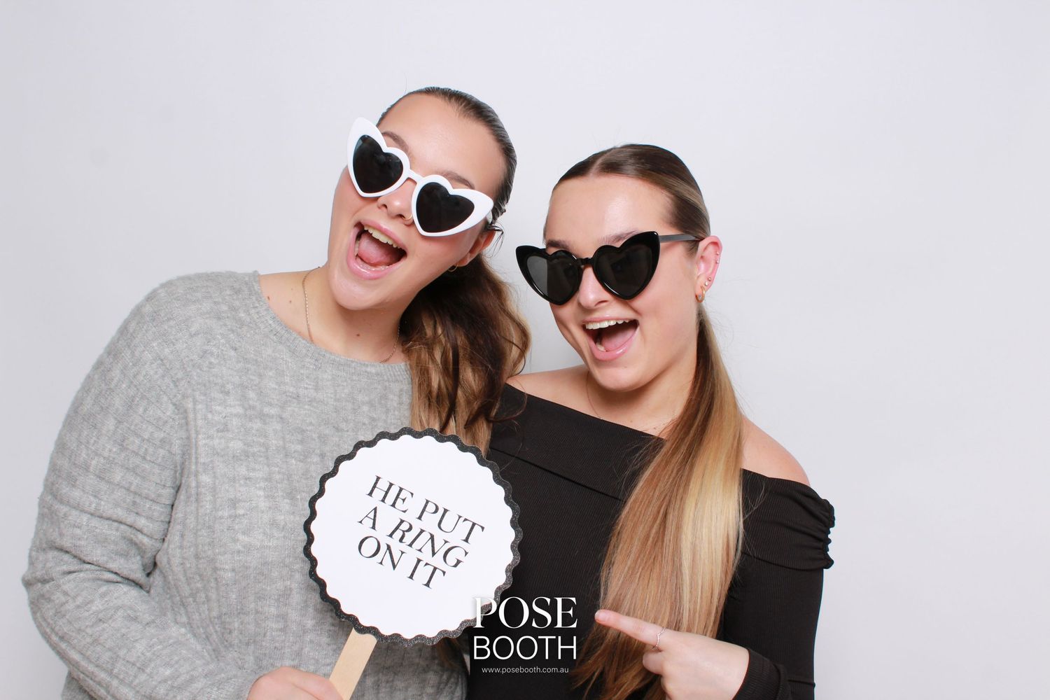 Two women in sunglasses and gray sweaters posing together at a photo booth with a speech bubble prop. Perth WA Photo booth Hire Event Booth