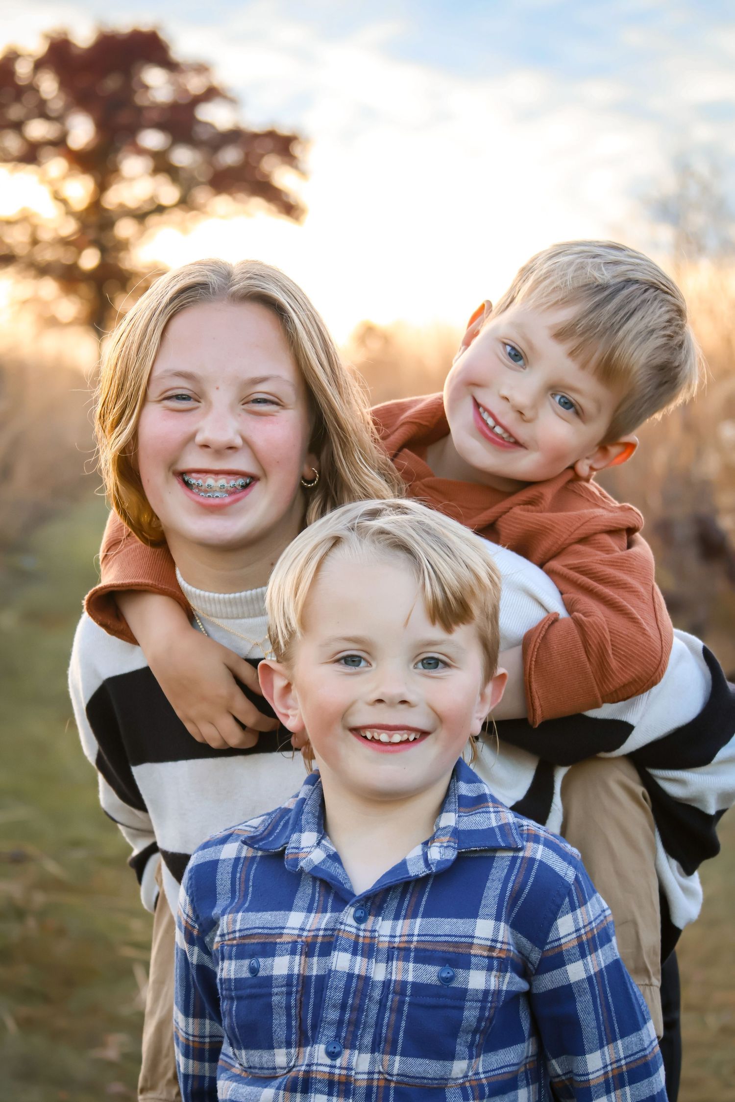 Three smiling kids on a trail path with the sun setting in the background