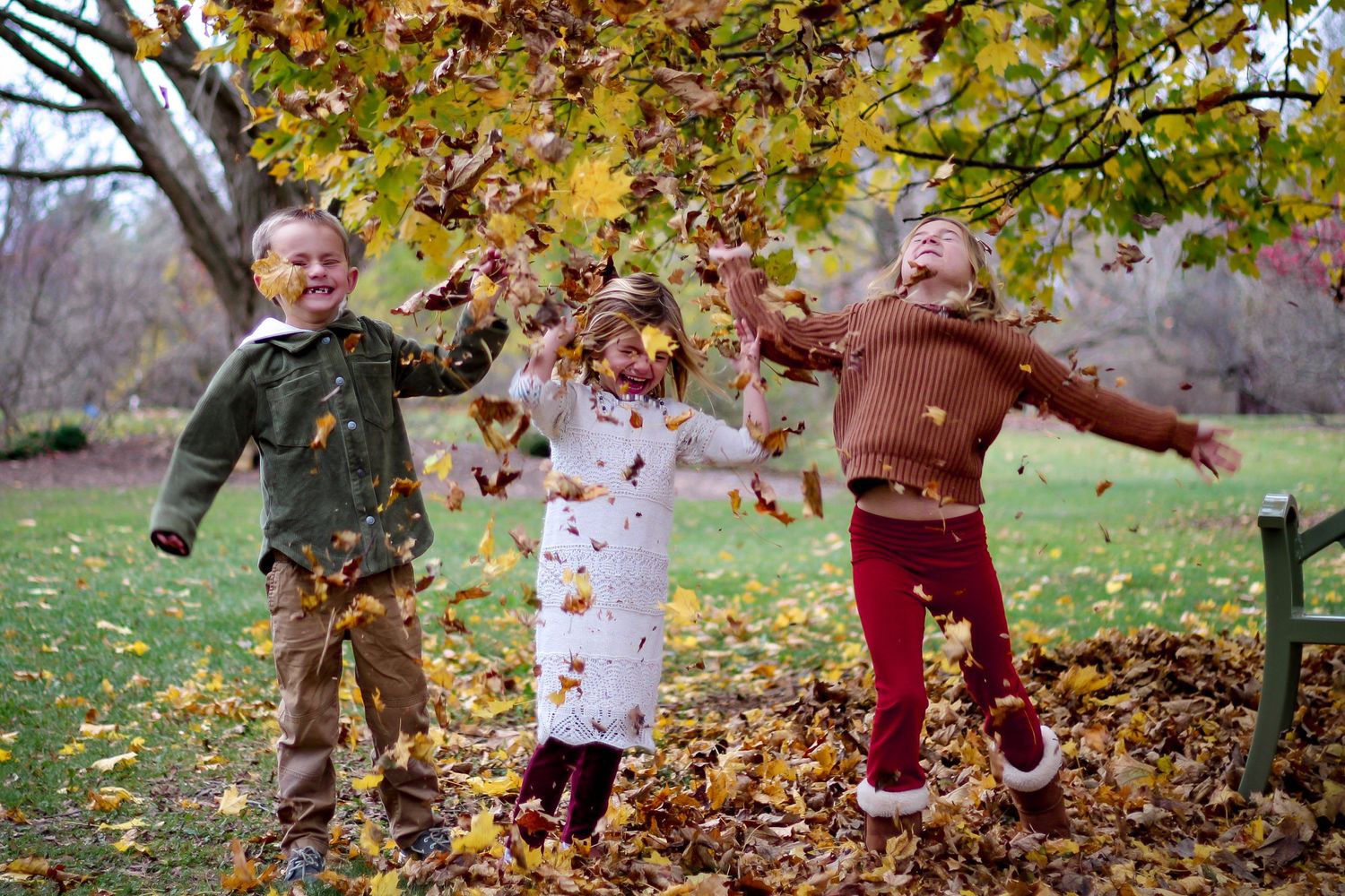 Three young kids having fun throwing leaves in the air