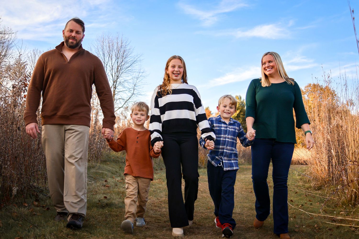Smiling family of five walking hand-in-hand on a grassy trail
