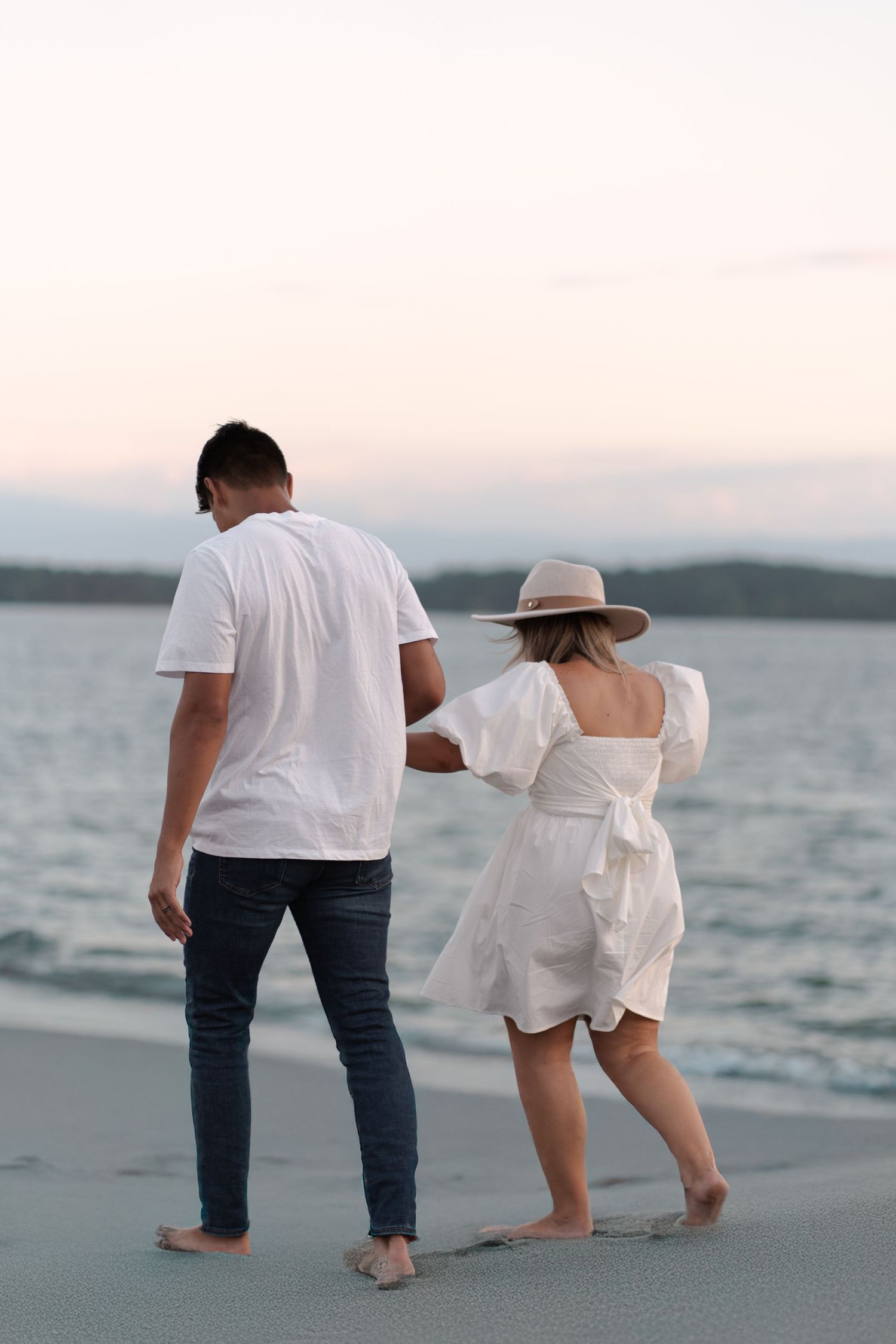 A couple takes a romantic barefoot walk along the beach at sunset.