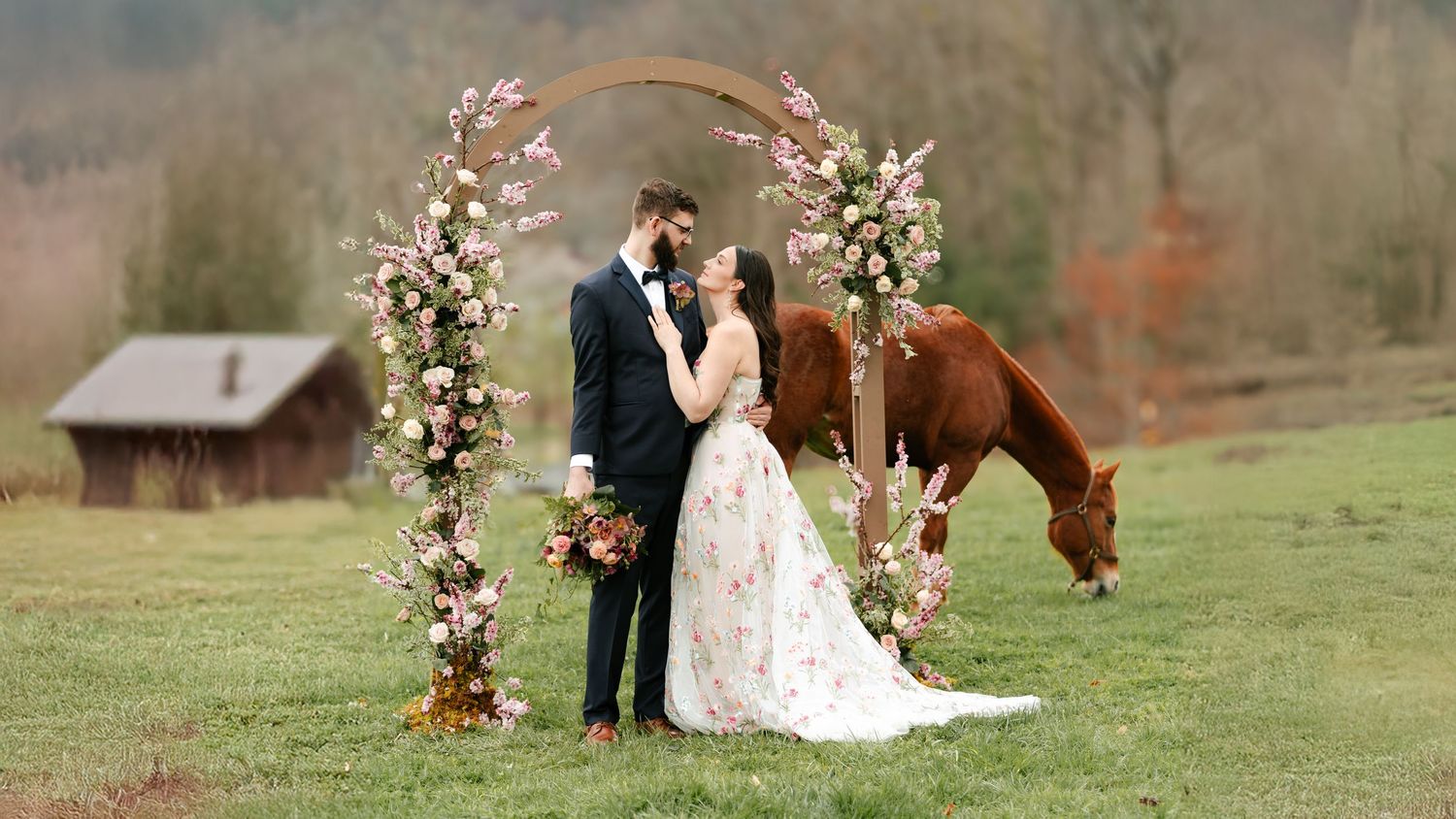 A wedding ceremony setup with floral arch and horse grazing in rustic countryside setting.