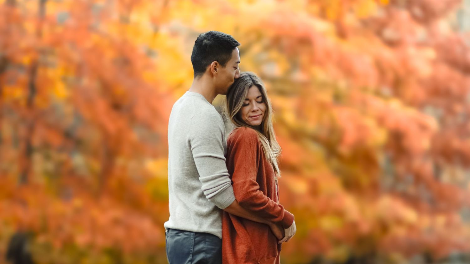 A romantic autumn scene with vibrant orange foliage in the background.