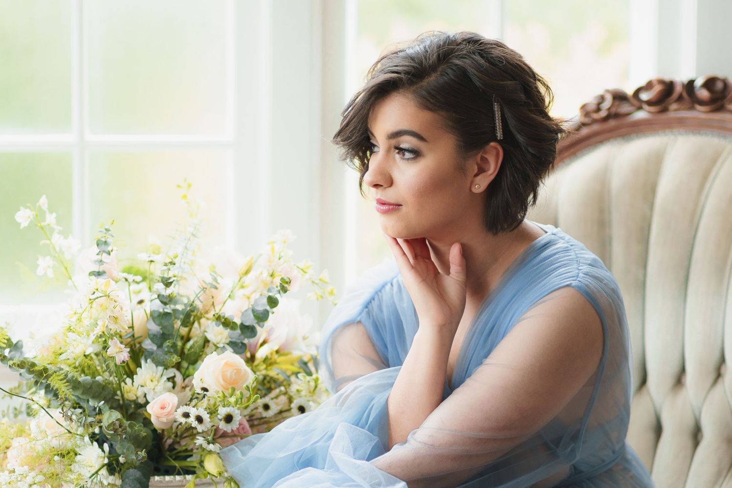 A dreamy portrait in soft blue featuring floral arrangements by a window.