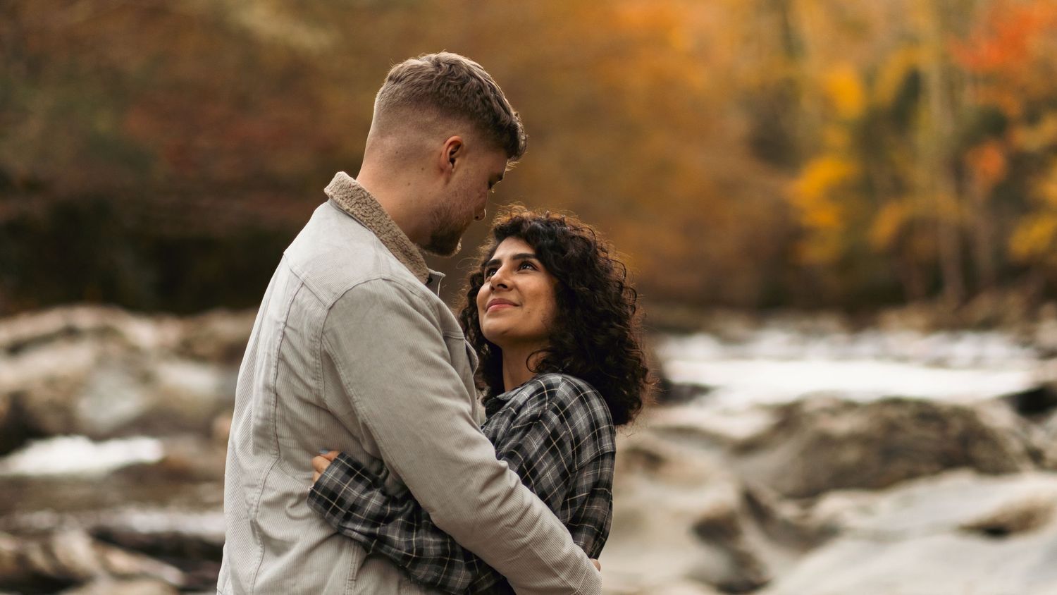 A romantic autumn moment captured by a stream with orange and red fall colors in the background.