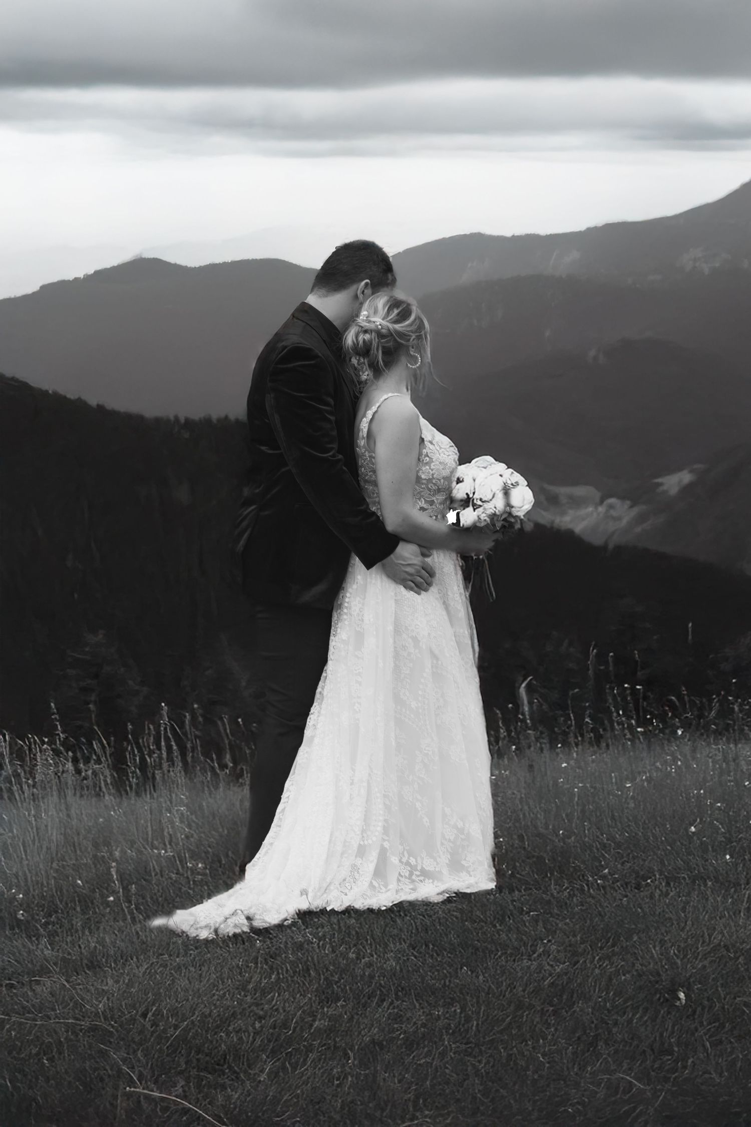 A romantic black and white wedding portrait on a mountaintop with dramatic cloudy skies.