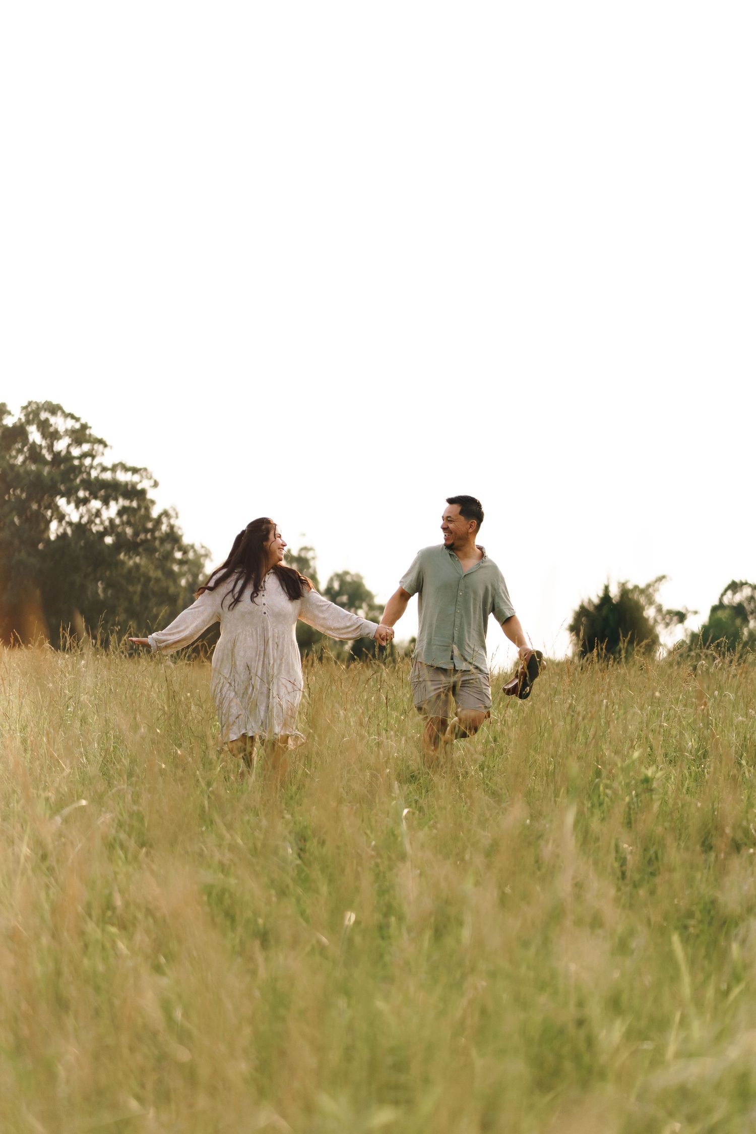 A couple holds hands while walking through a serene meadow of tall grass during golden hour.