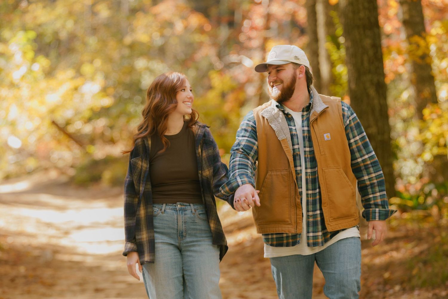 Couple walking hand in hand on autumn forest path surrounded by golden fall foliage.