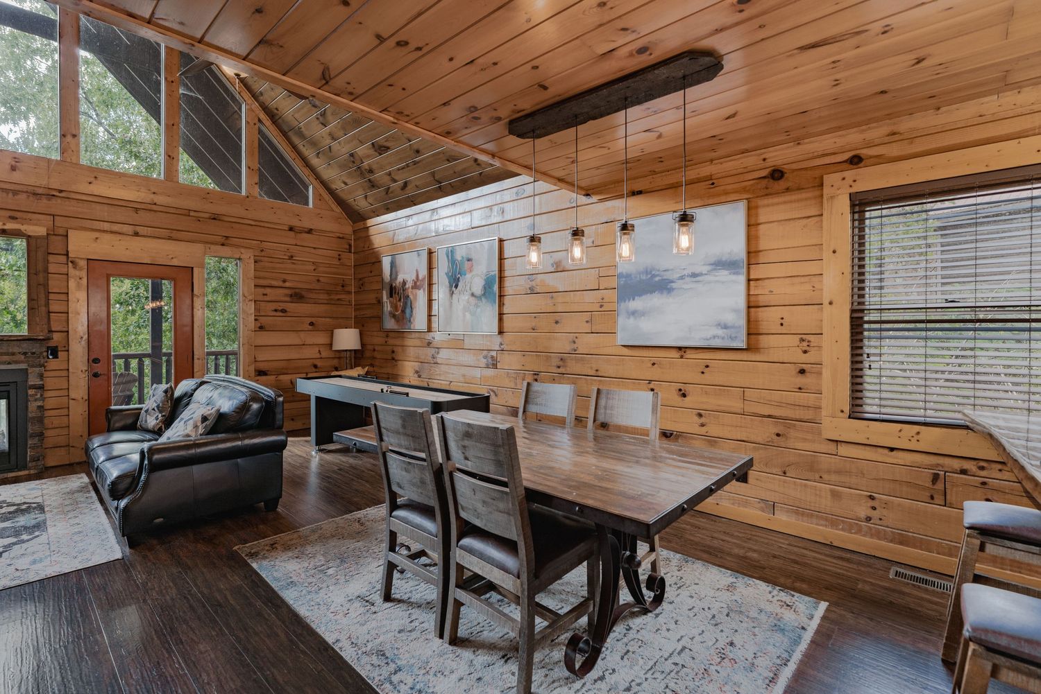 Rustic cabin dining room with wood paneled walls and modern pendant lighting.